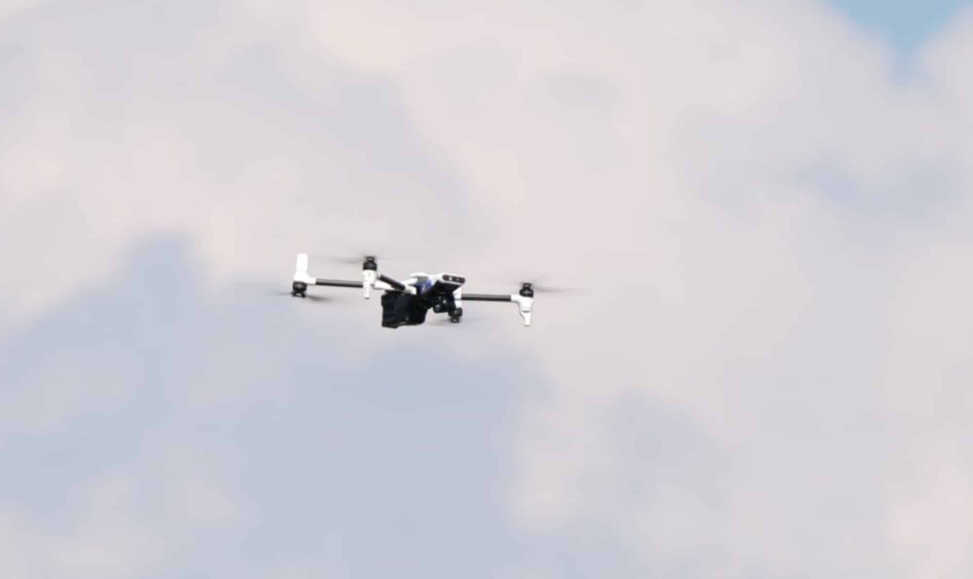 Small fixed-wing-style quadcopter flying against a pale overcast sky.