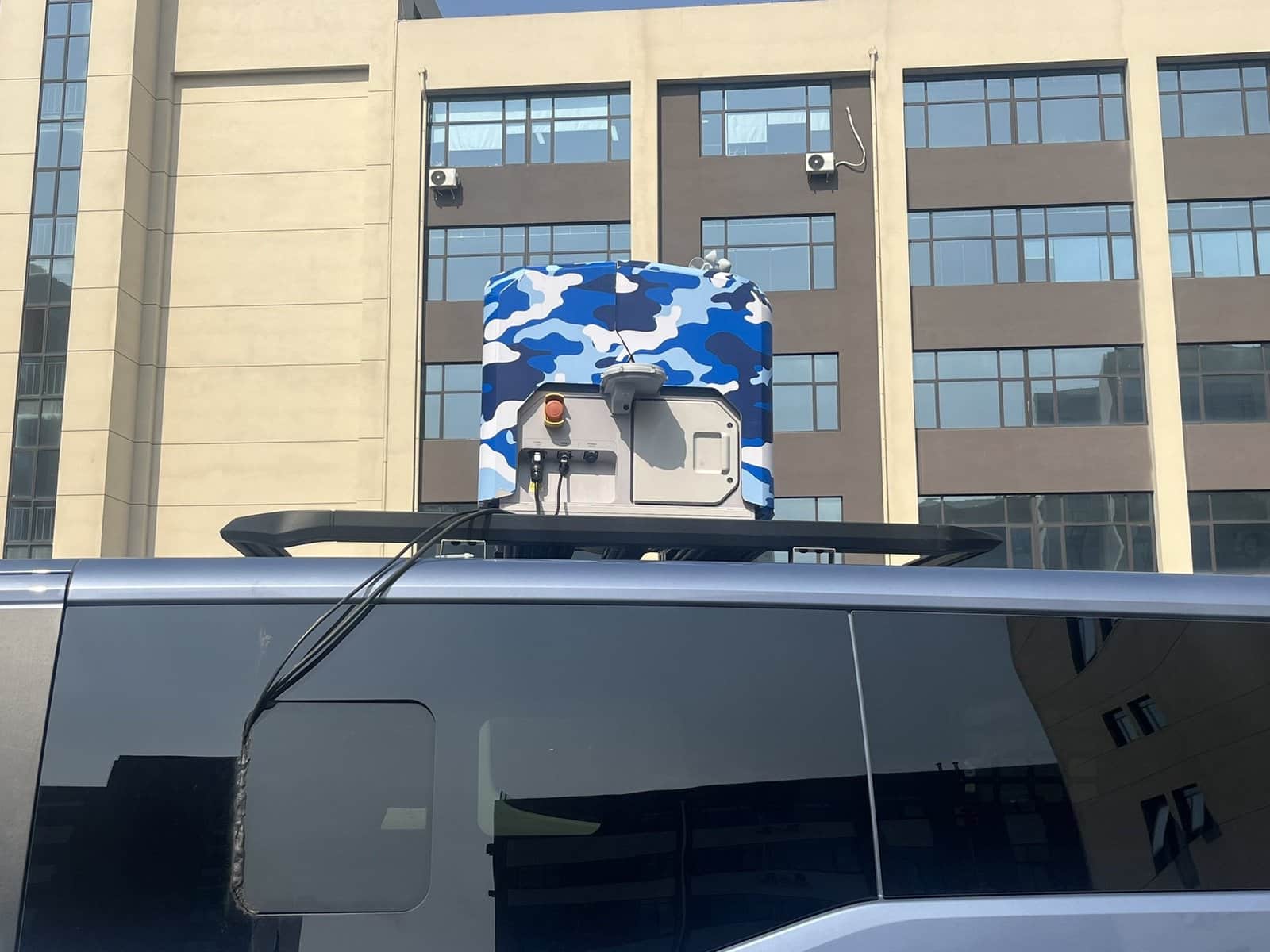 Blue camouflage-wrapped dock mounted on a van roof outside an office building.