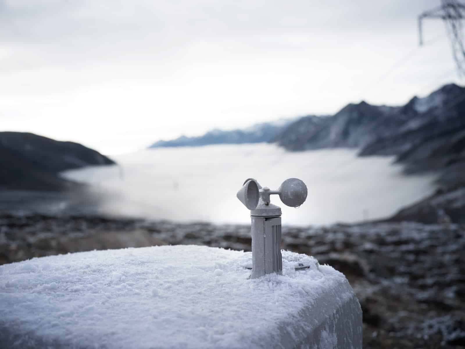 Anemometer spinning on a snow-dusted dock lid above a frozen mountain lake.