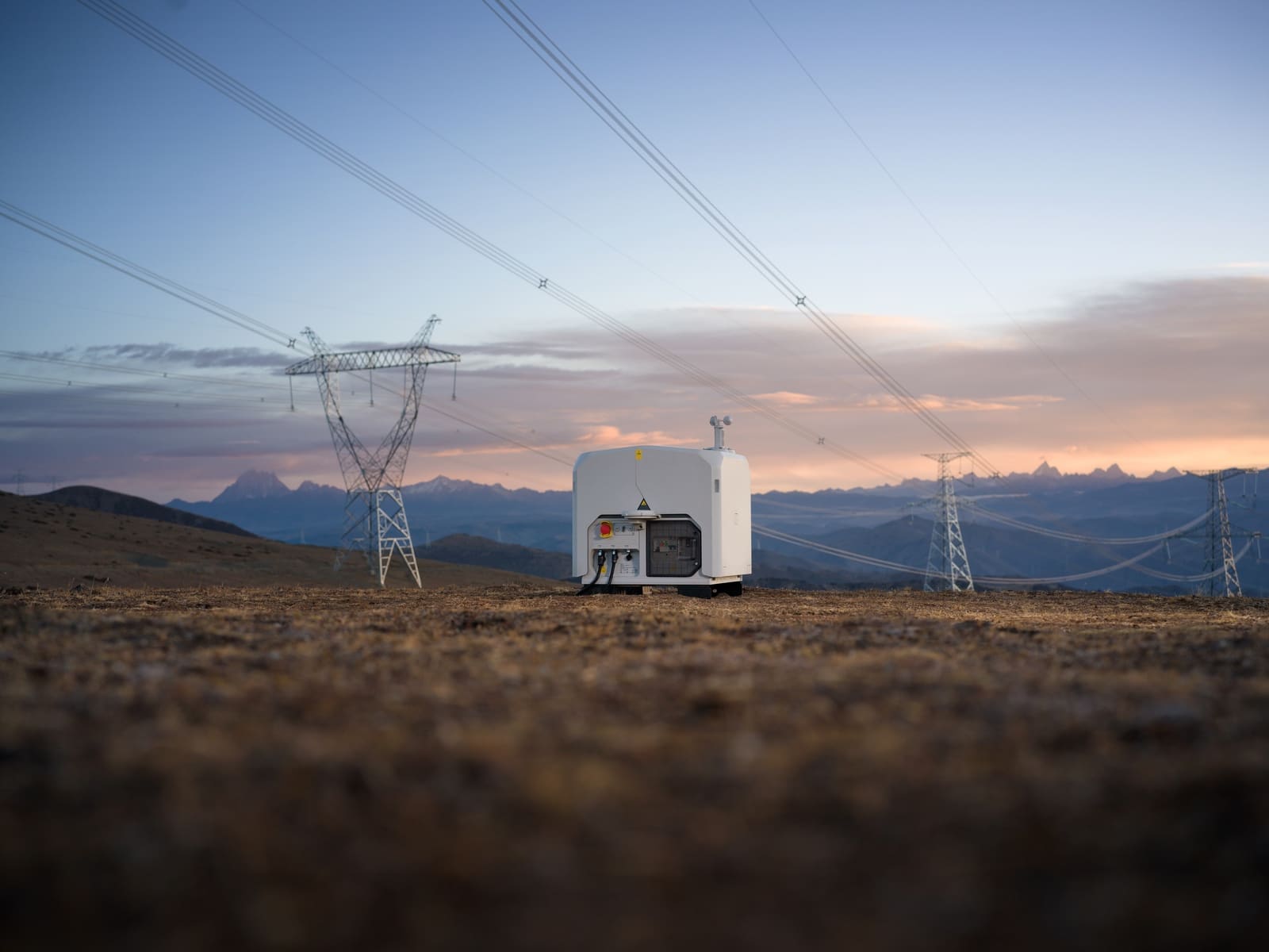 Closed dock parked on brown grassland directly beneath high-voltage conductors.