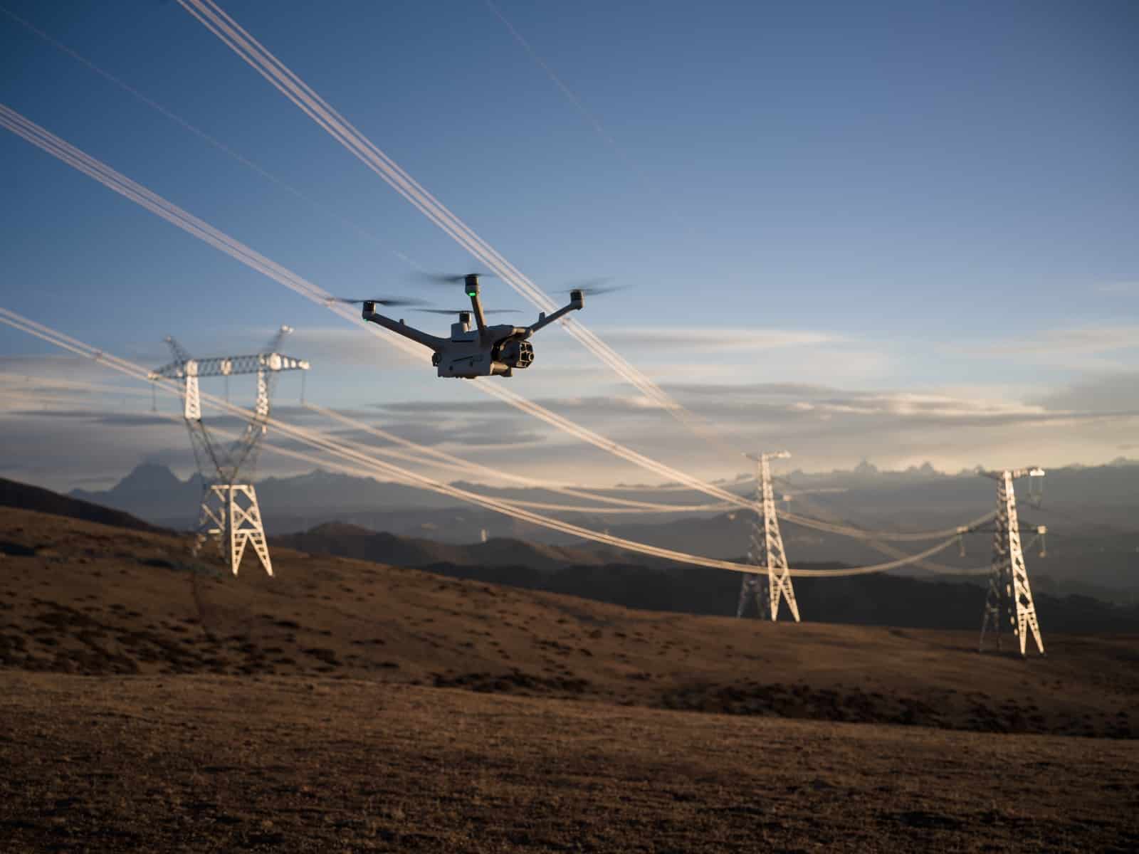 Drone silhouetted against a dusk sky among widely spaced power pylons.