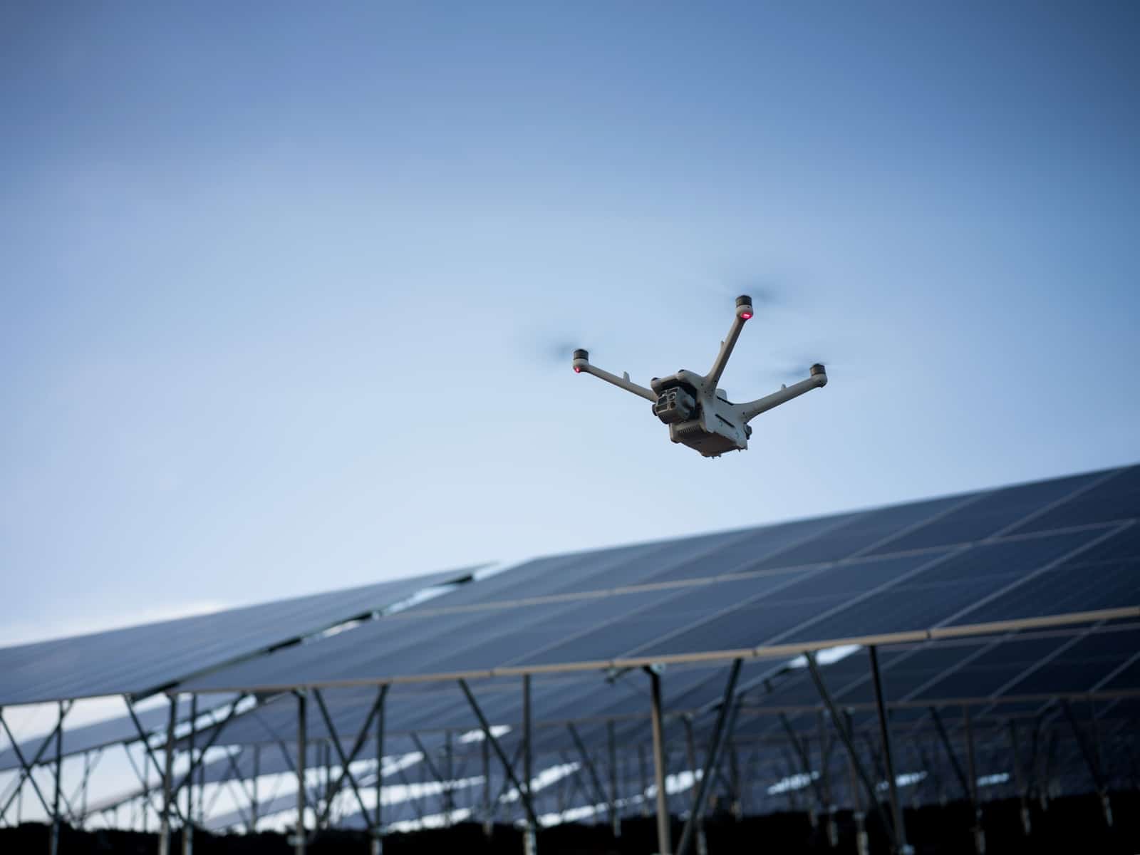 Drone passing low over an angled row of photovoltaic panels.
