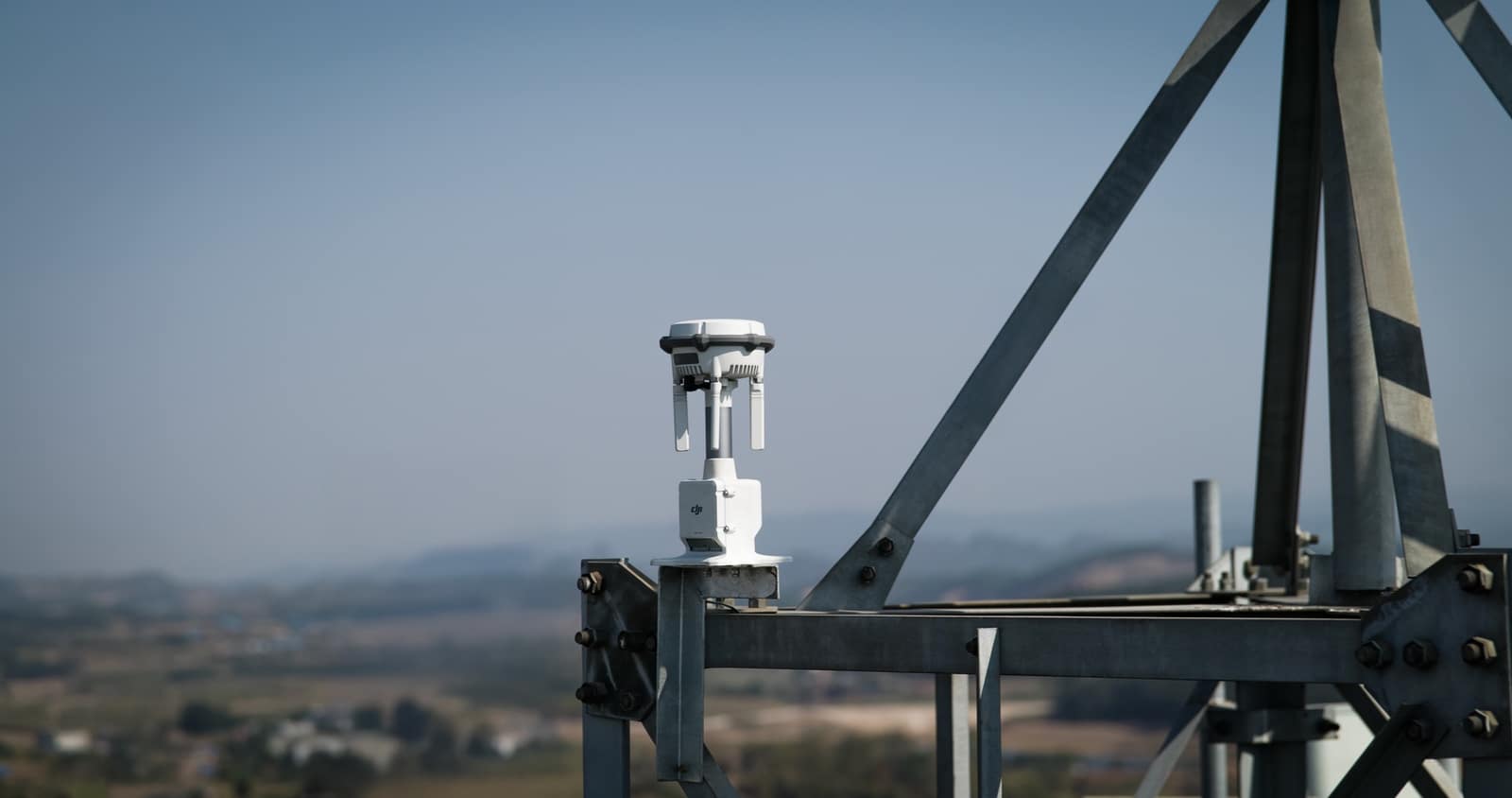 White sensor unit bolted to a steel lattice frame overlooking a valley.