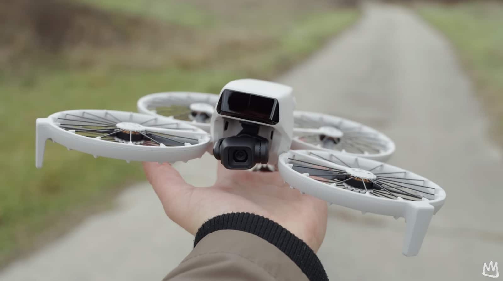A hand holds a caged DJI Flip above a gravel path.