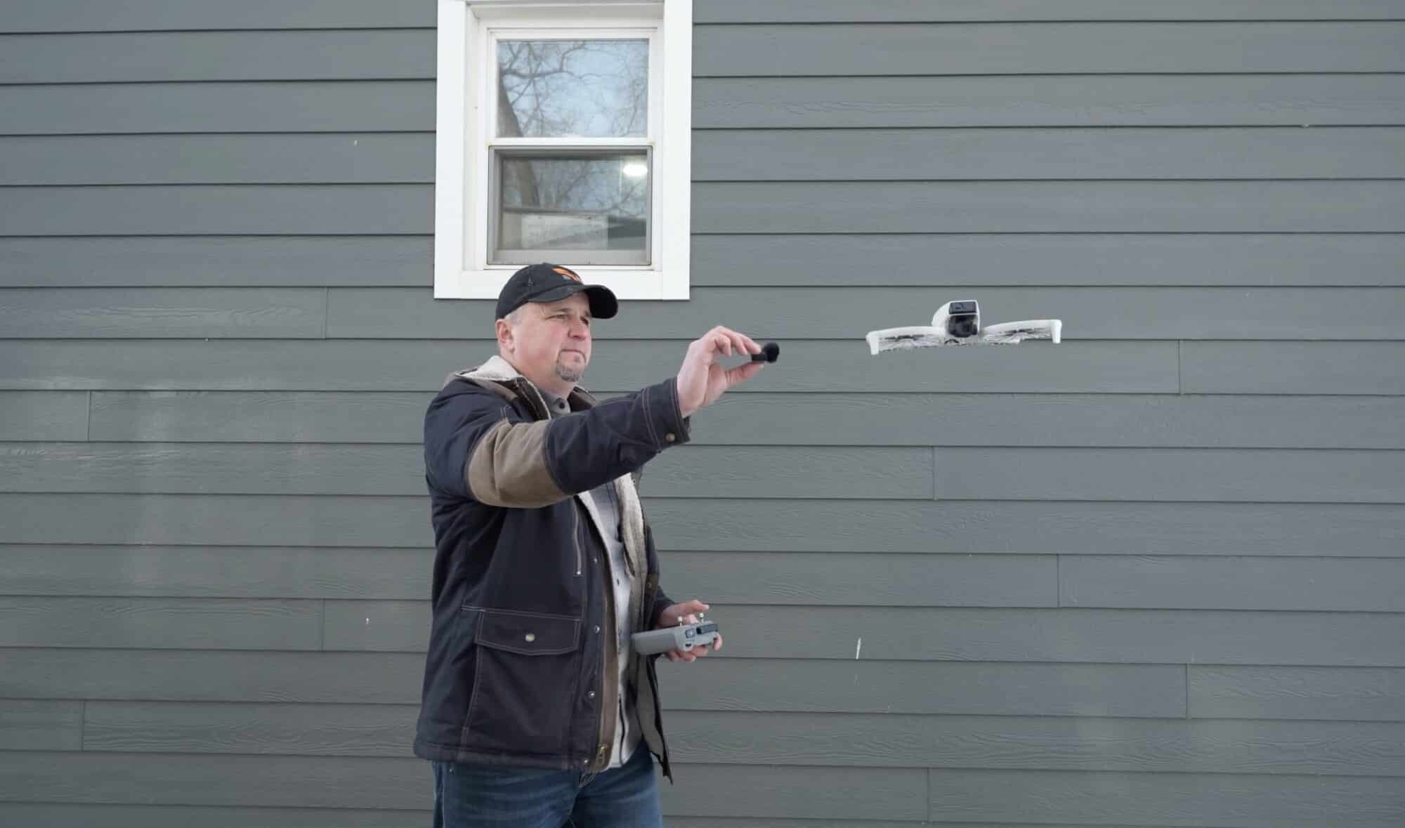 A small guarded quadcopter hovers next to the reviewer's outstretched microphone.