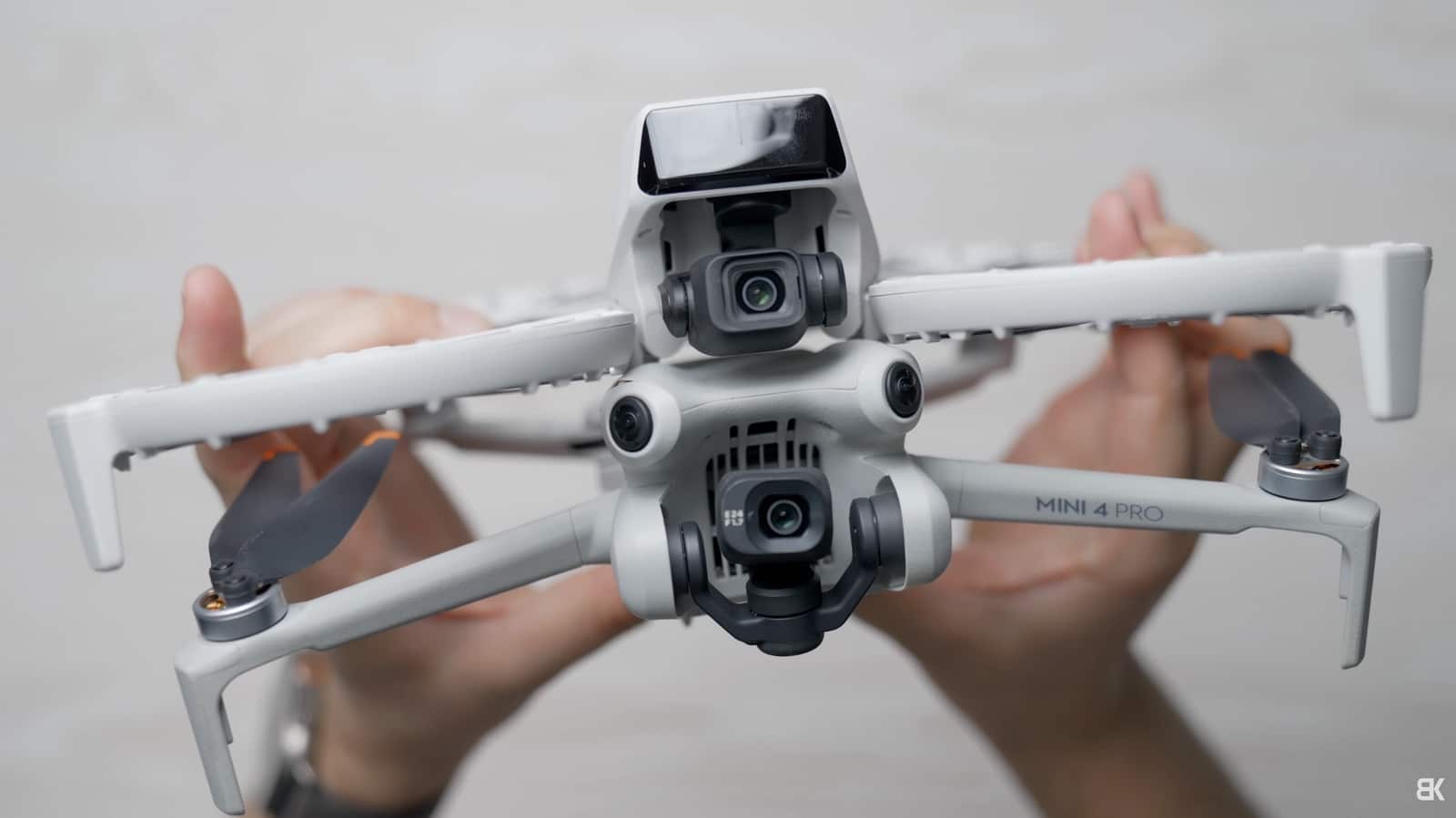 Hands hold a DJI Mini 4 Pro from below, showing gimbal and sensors.