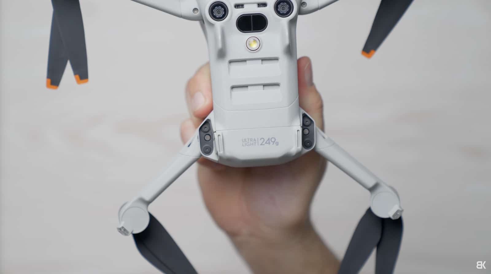 Hand holding a folded Mini 4 Pro from below with orange-tipped propellers.