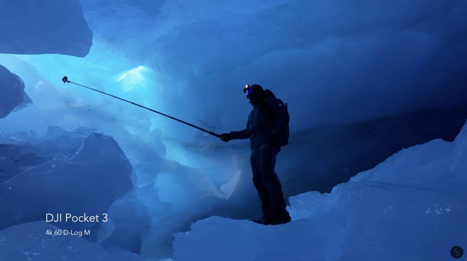 Silhouetted figure casting a fishing line inside a glowing blue ice cave.