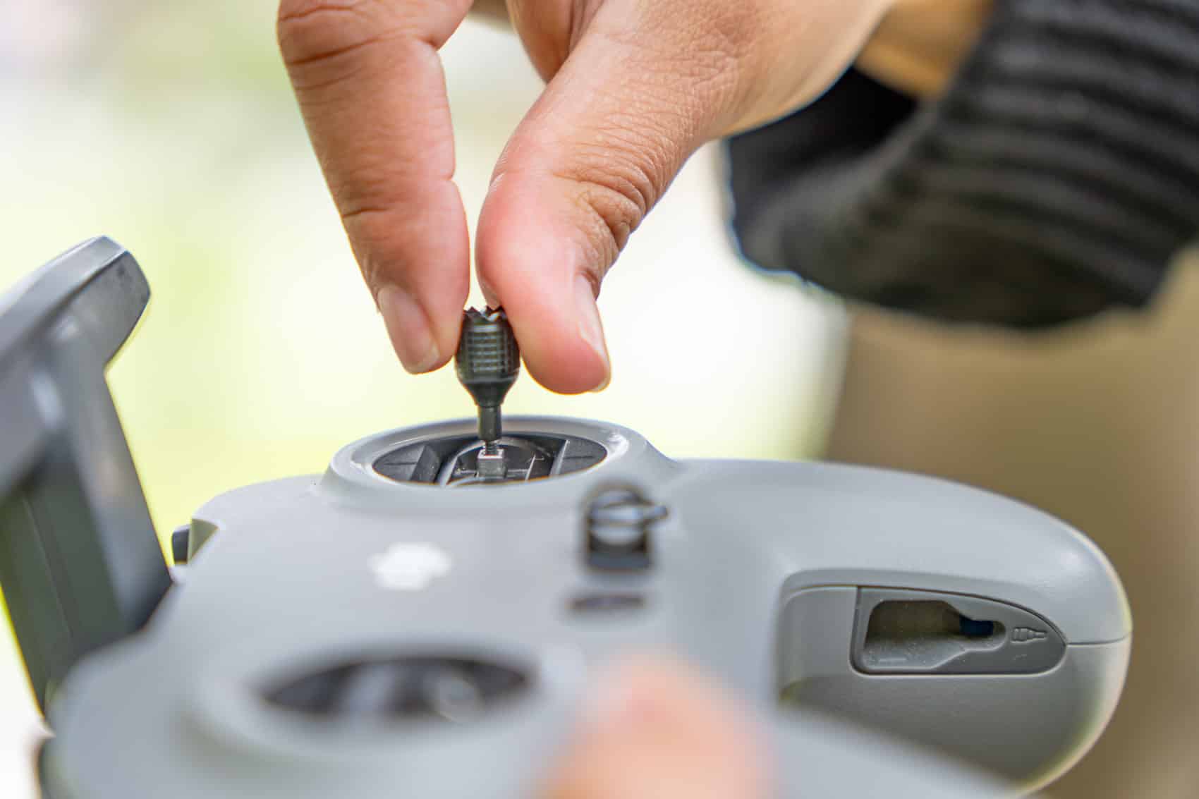 Fingers thread a control stick onto the gimbal of a grey drone remote.