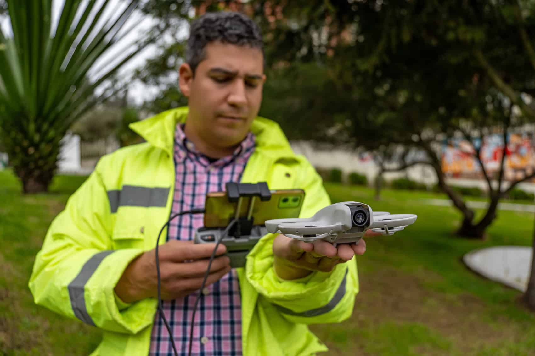 Man in a high-visibility jacket holding a small drone and controller outdoors.