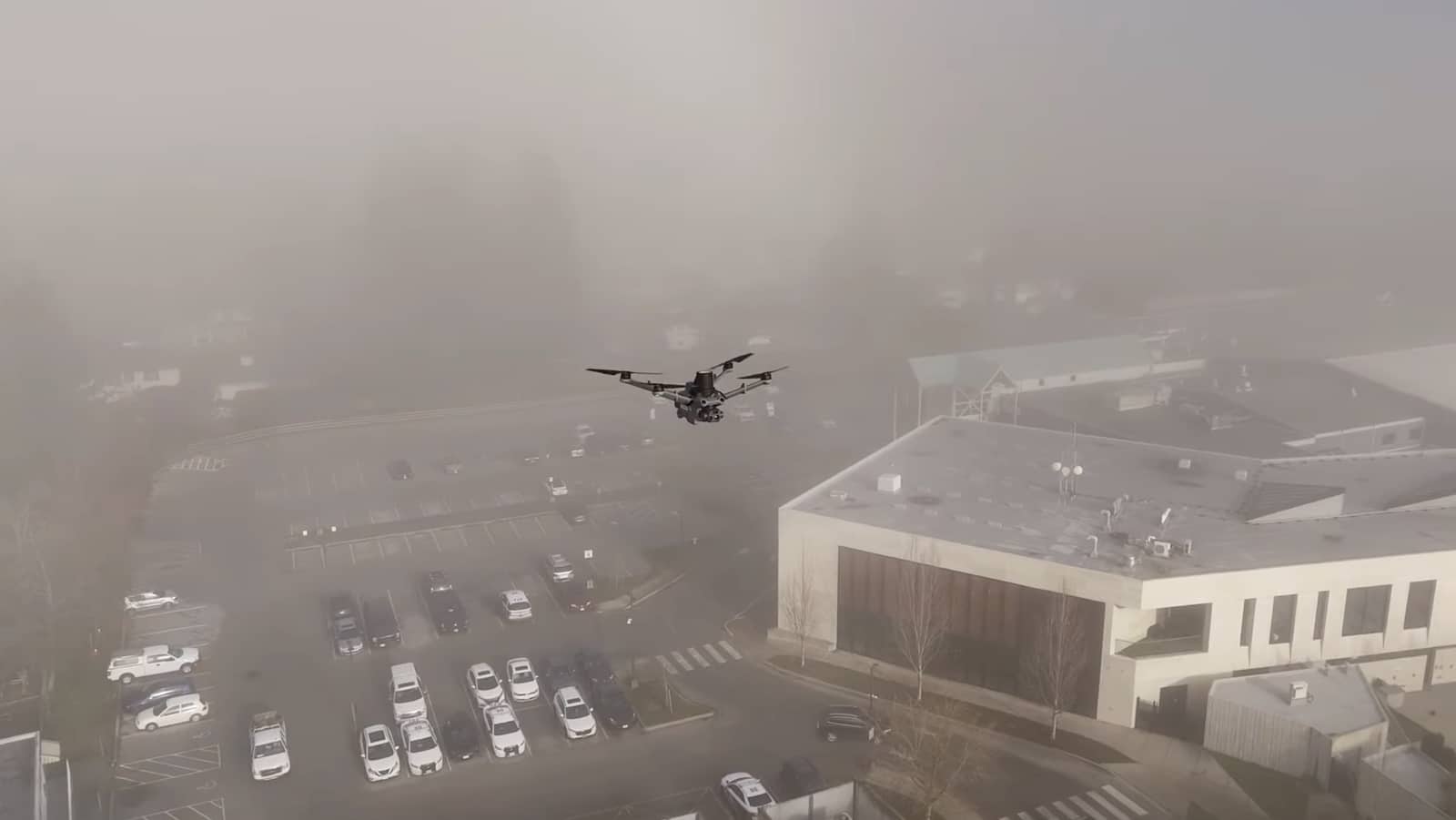 Aerial view of a fog-shrouded town with a drone silhouetted above the rooftops.