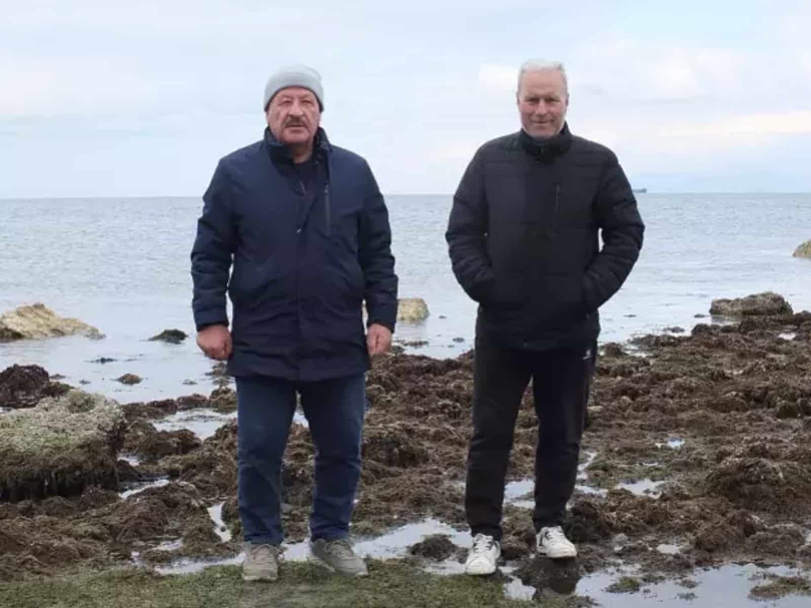 Two men stand on the seabed exposed after the Aegean pulled back from shore.