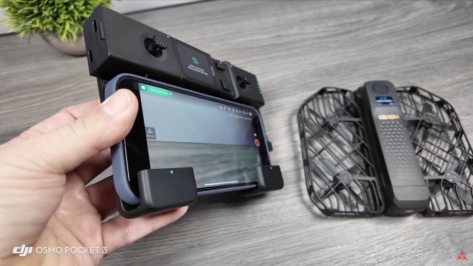 Hand holding a phone clipped into the controller with the folded drone nearby.