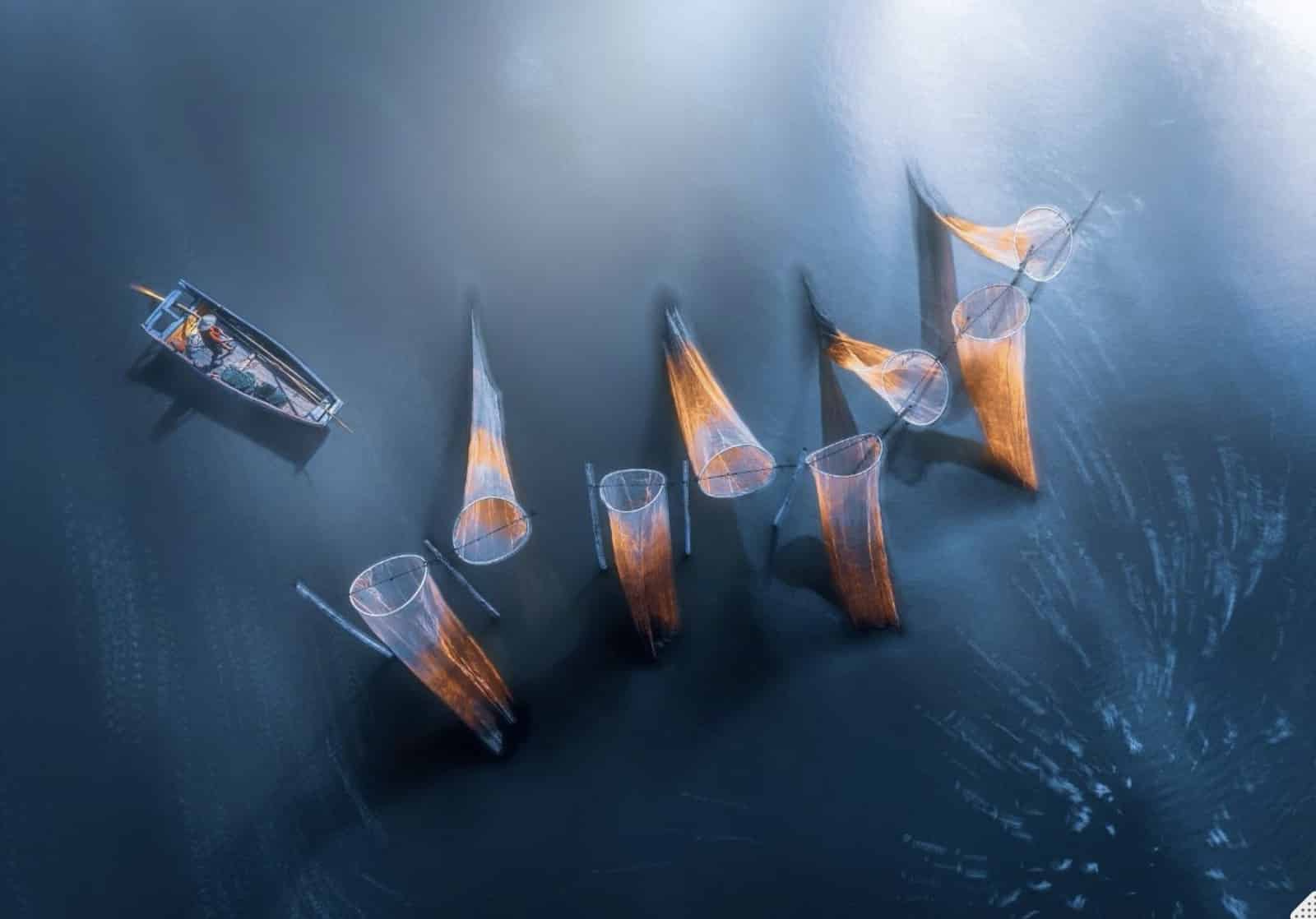 Overhead view of orange fish traps drifting in dark water beside a boat.