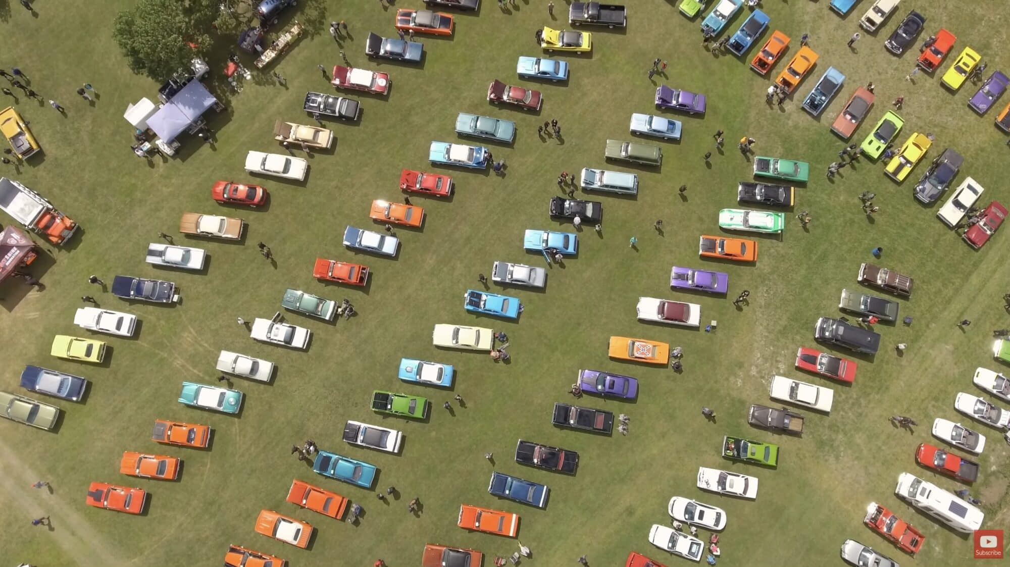 Top-down aerial of rows of colorful classic cars parked on grass at a show.