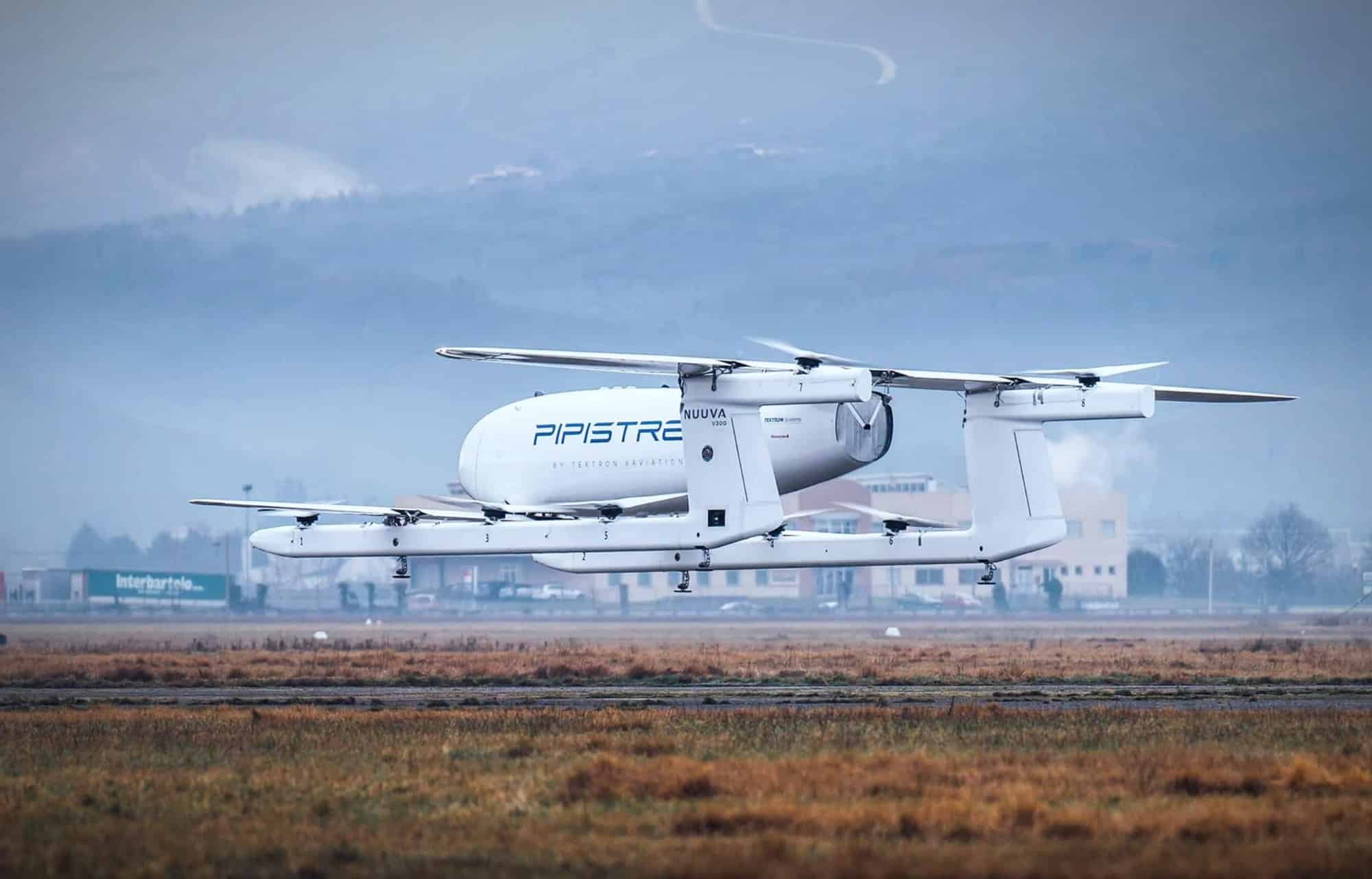 The white cargo VTOL hovers on its lift rotors above a winter airfield.