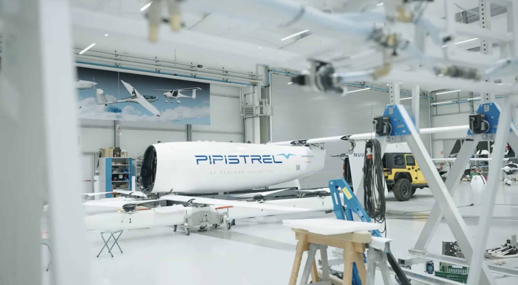 The aircraft sits in a bright assembly hall surrounded by work stands.
