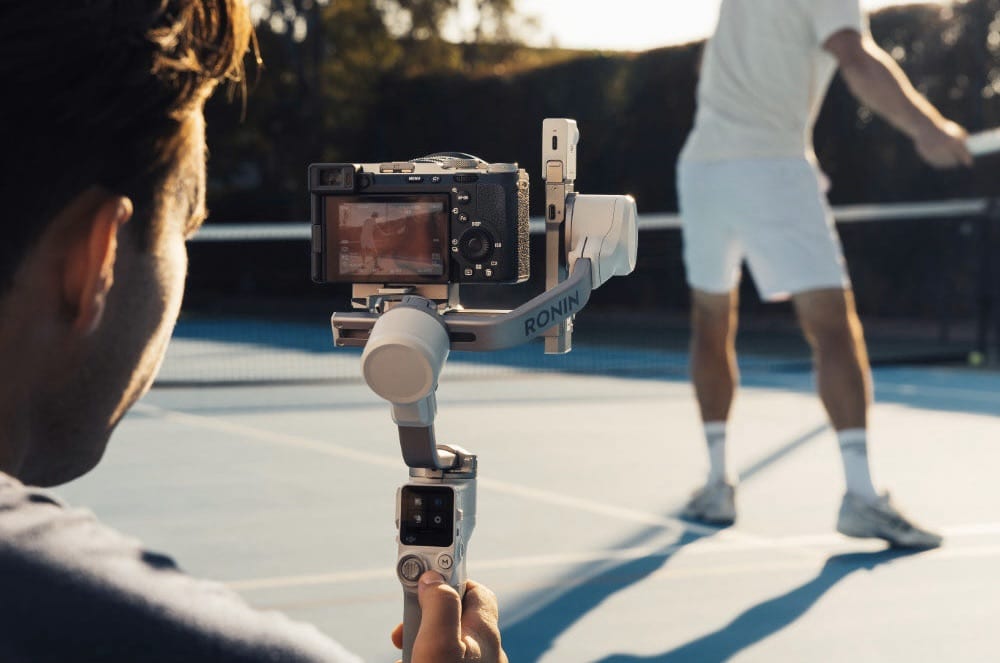 An operator films a racquet player from courtside using a Ronin gimbal rig.