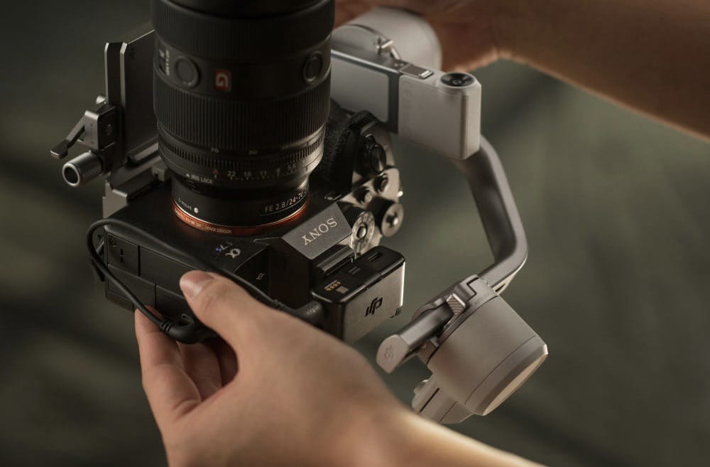 Hands grip the gimbal handle beneath a full-frame camera and a large lens.