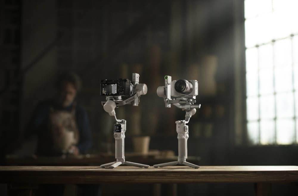 Two Ronin gimbals, one black and one white, stand on a sunlit workshop table.