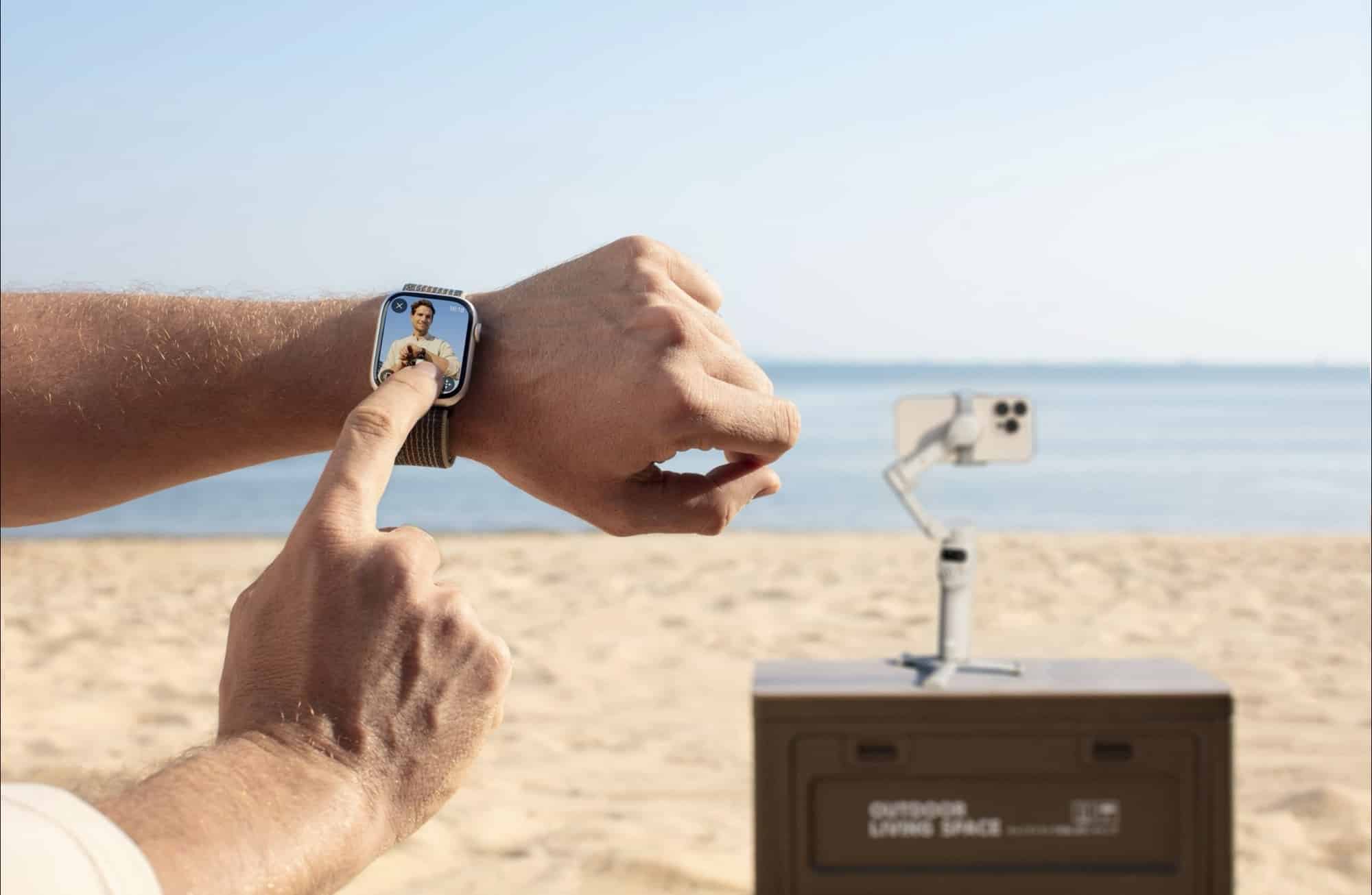 A wrist-worn screen previews the shot while the gimbal films from a crate.