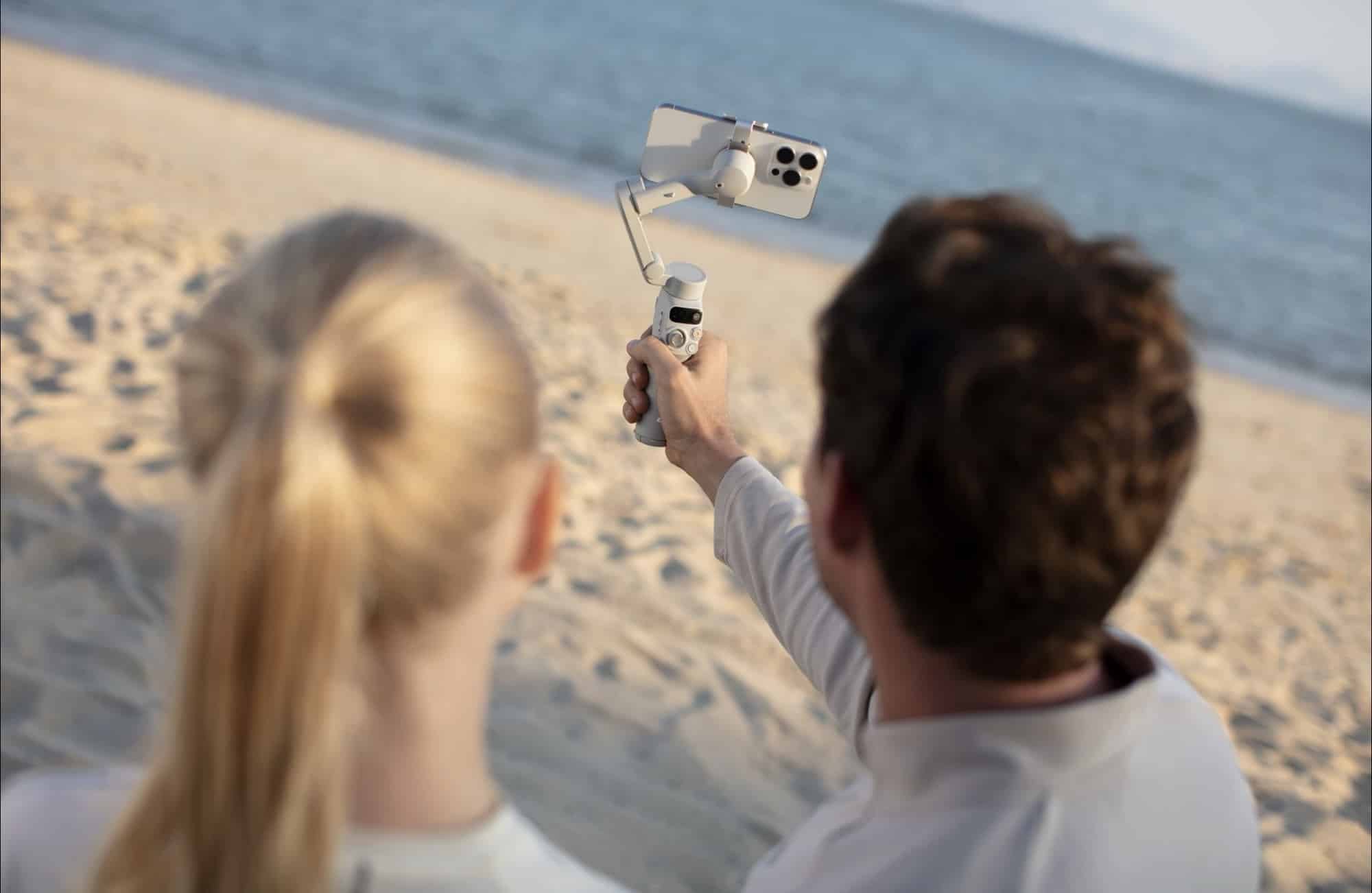 A man and a girl watch the phone on the gimbal he holds at the shore.