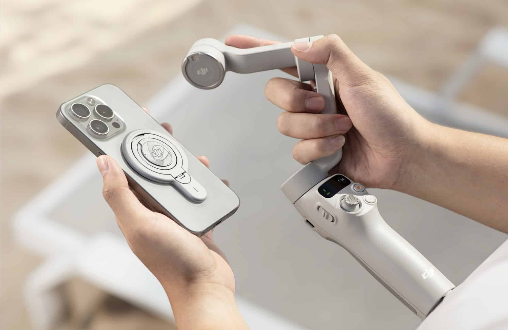 Hands clip a phone into the magnetic clamp on the light gray gimbal.