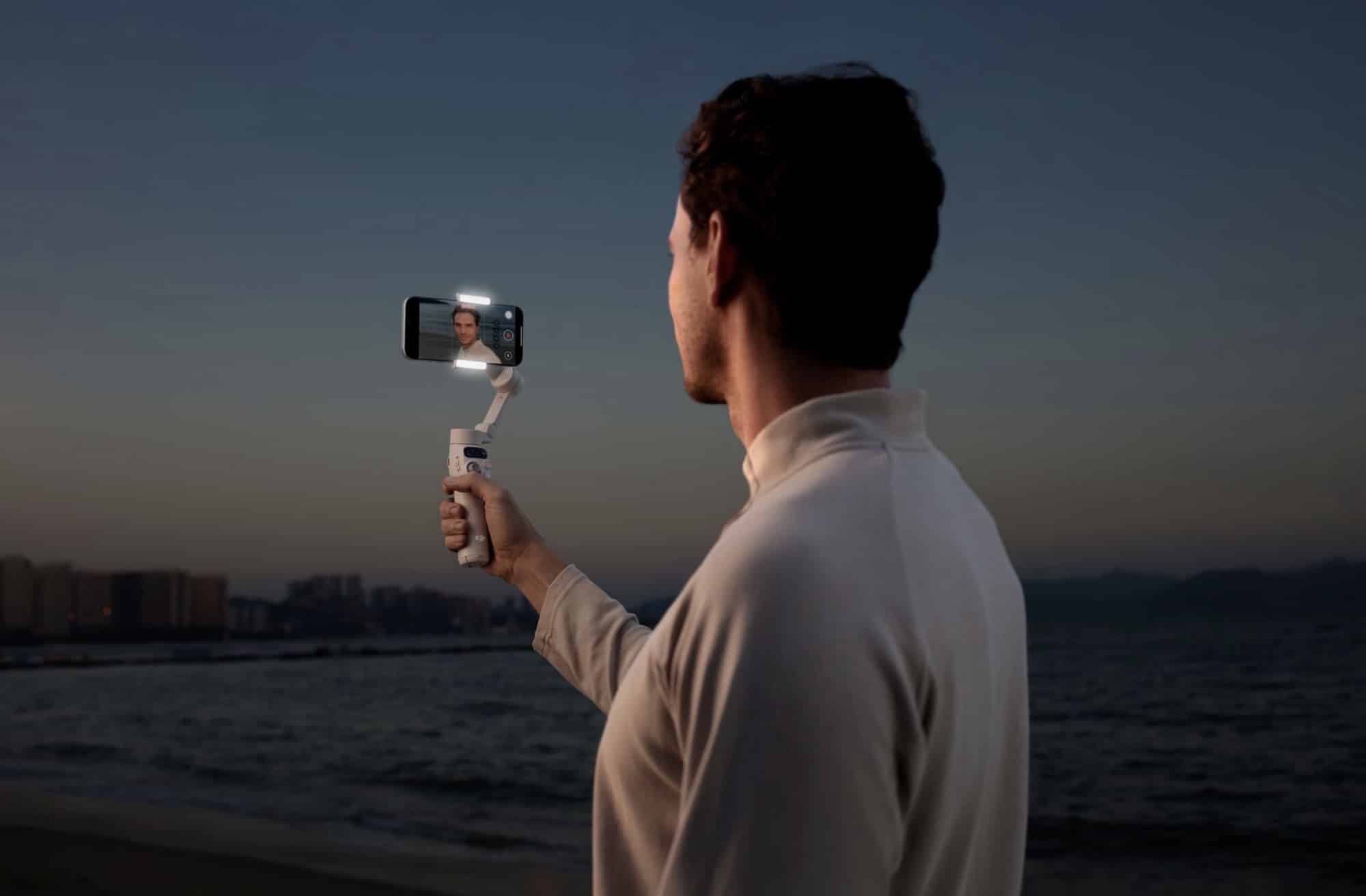 A man self-films with the gimbal at arm length as dusk falls over the sea.