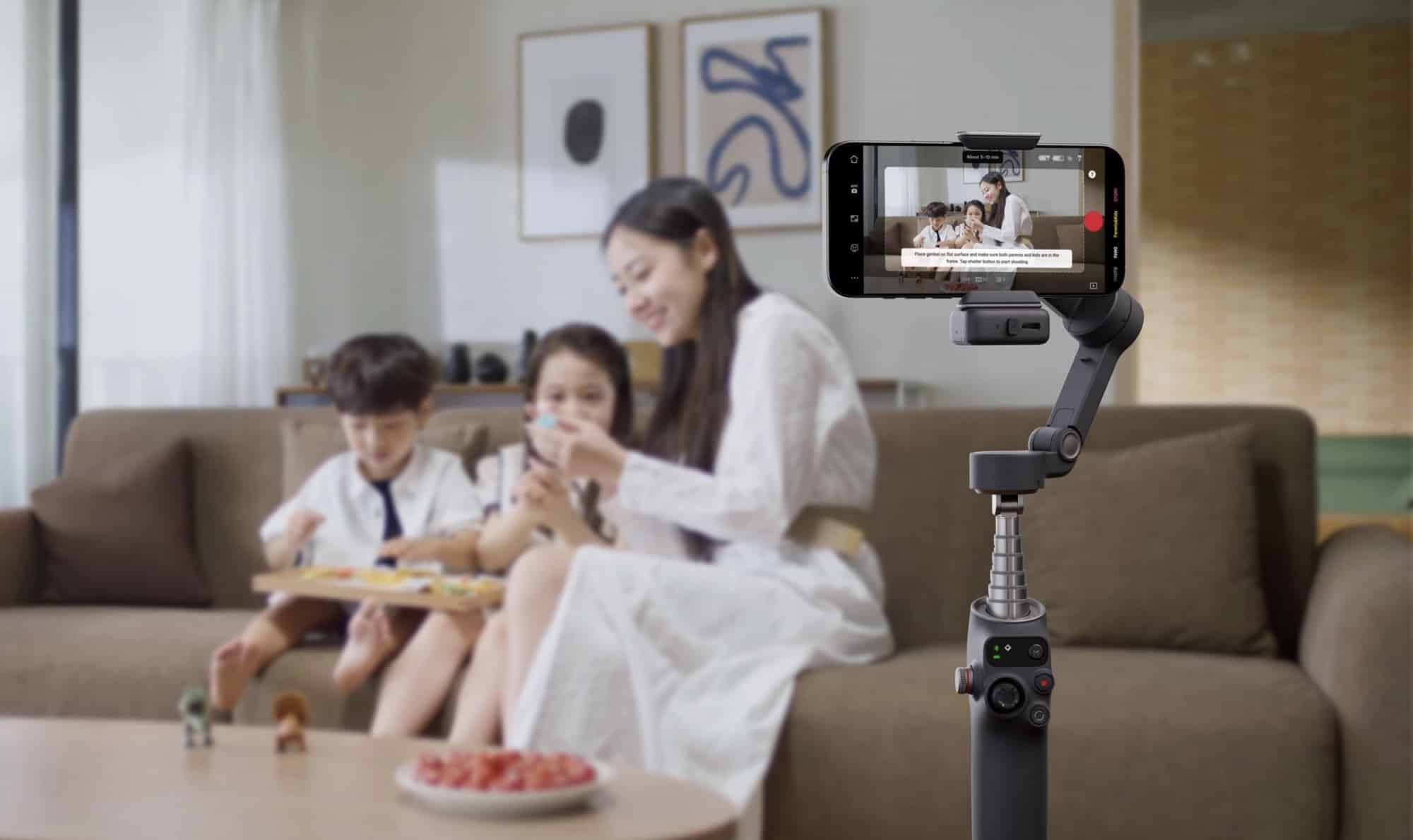 A gimbal on a table films a family sharing snacks on a living room sofa.