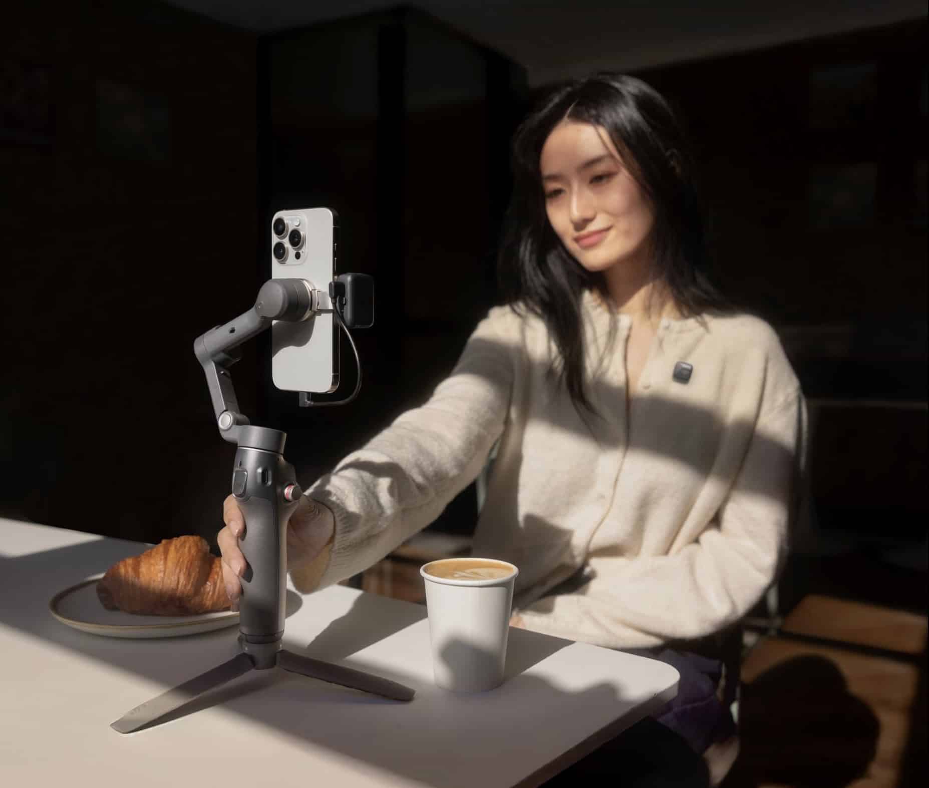 A woman reaches toward the tripod-mounted gimbal across a cafe table.