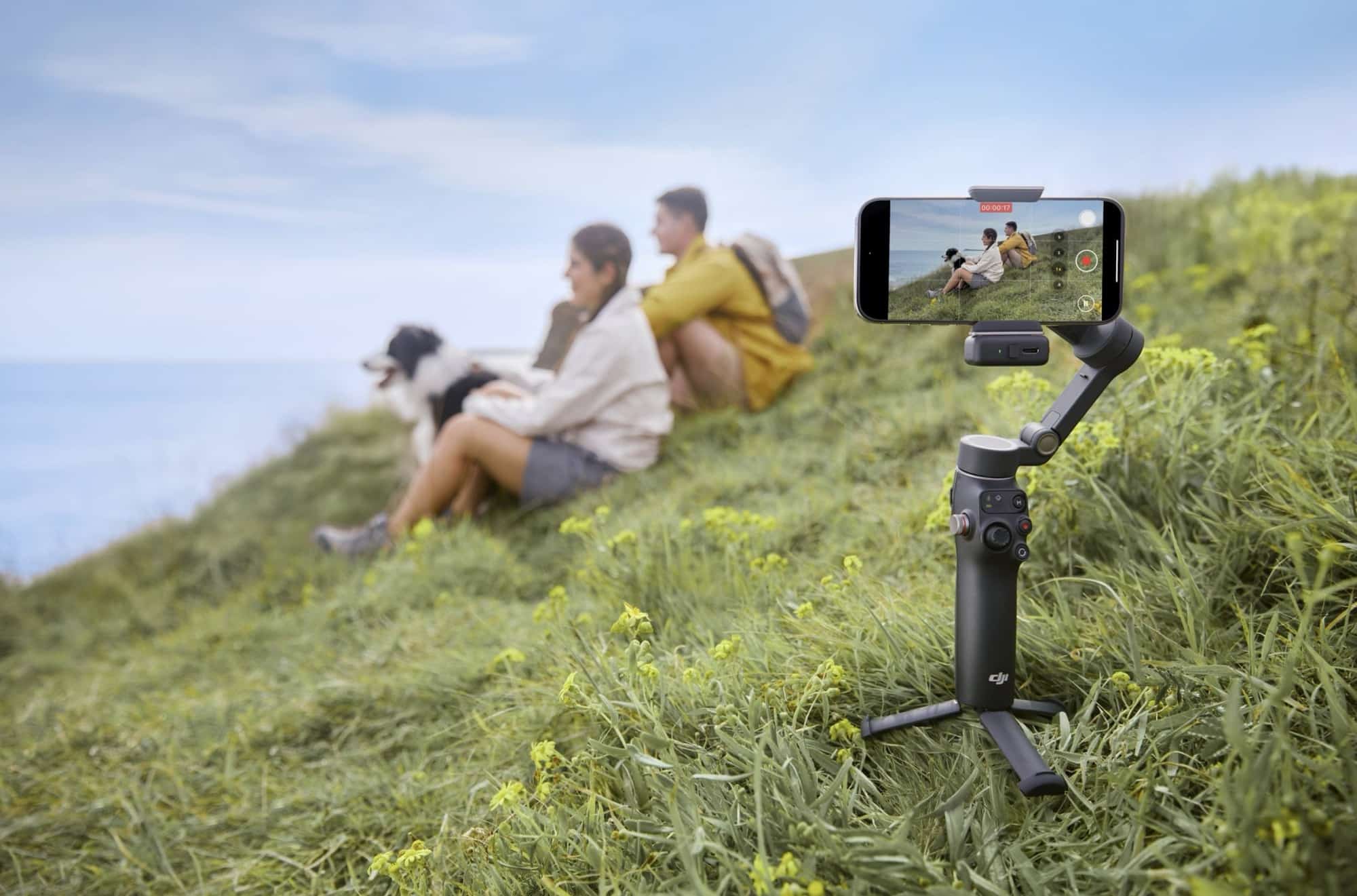 A gimbal planted in grass films a family seated on a green hillside.