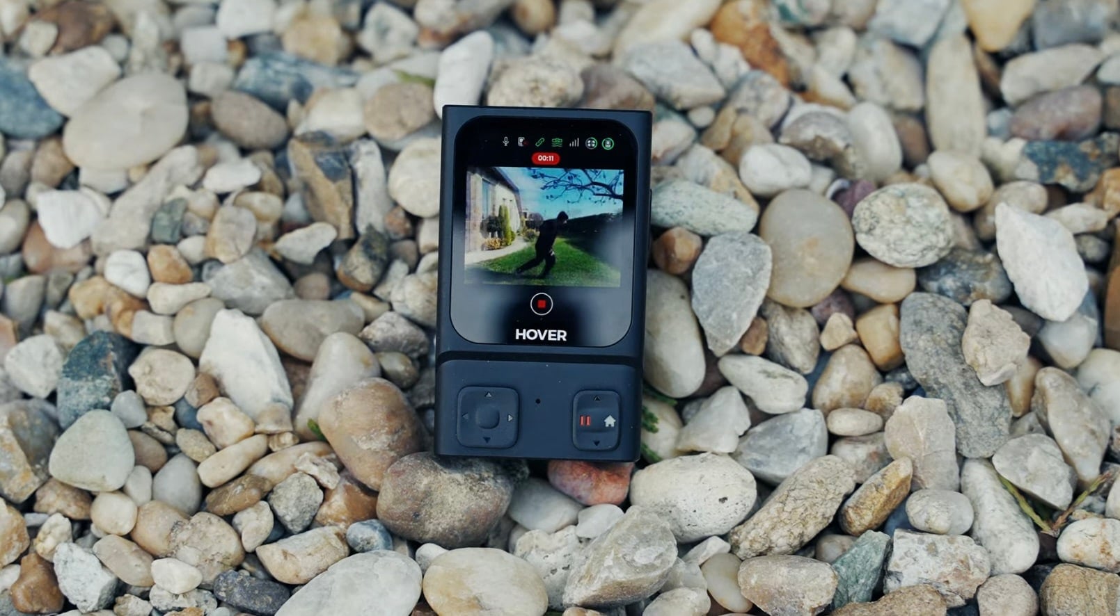 The beacon lies on gravel showing its live camera preview and control buttons.