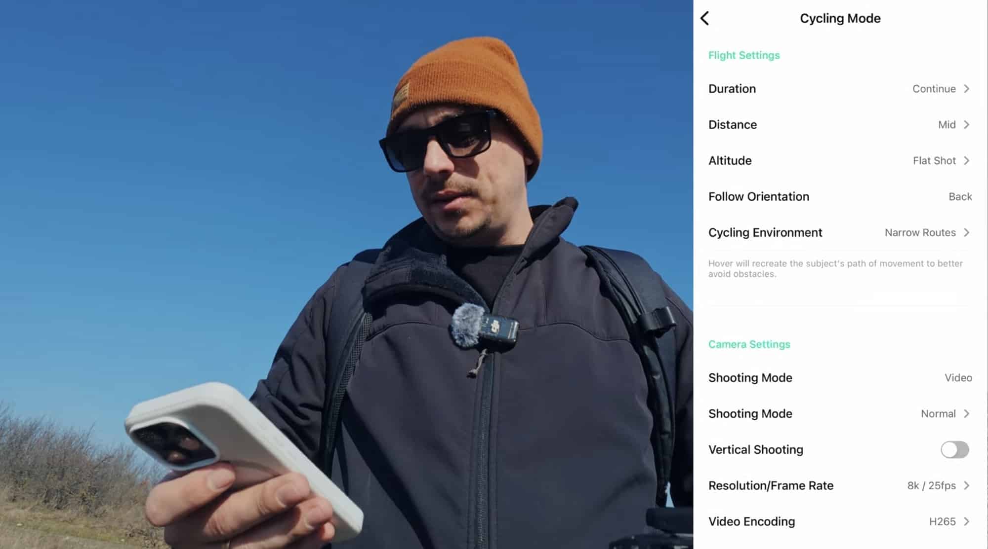 The reviewer in an orange beanie holds a phone showing the cycling mode menu.