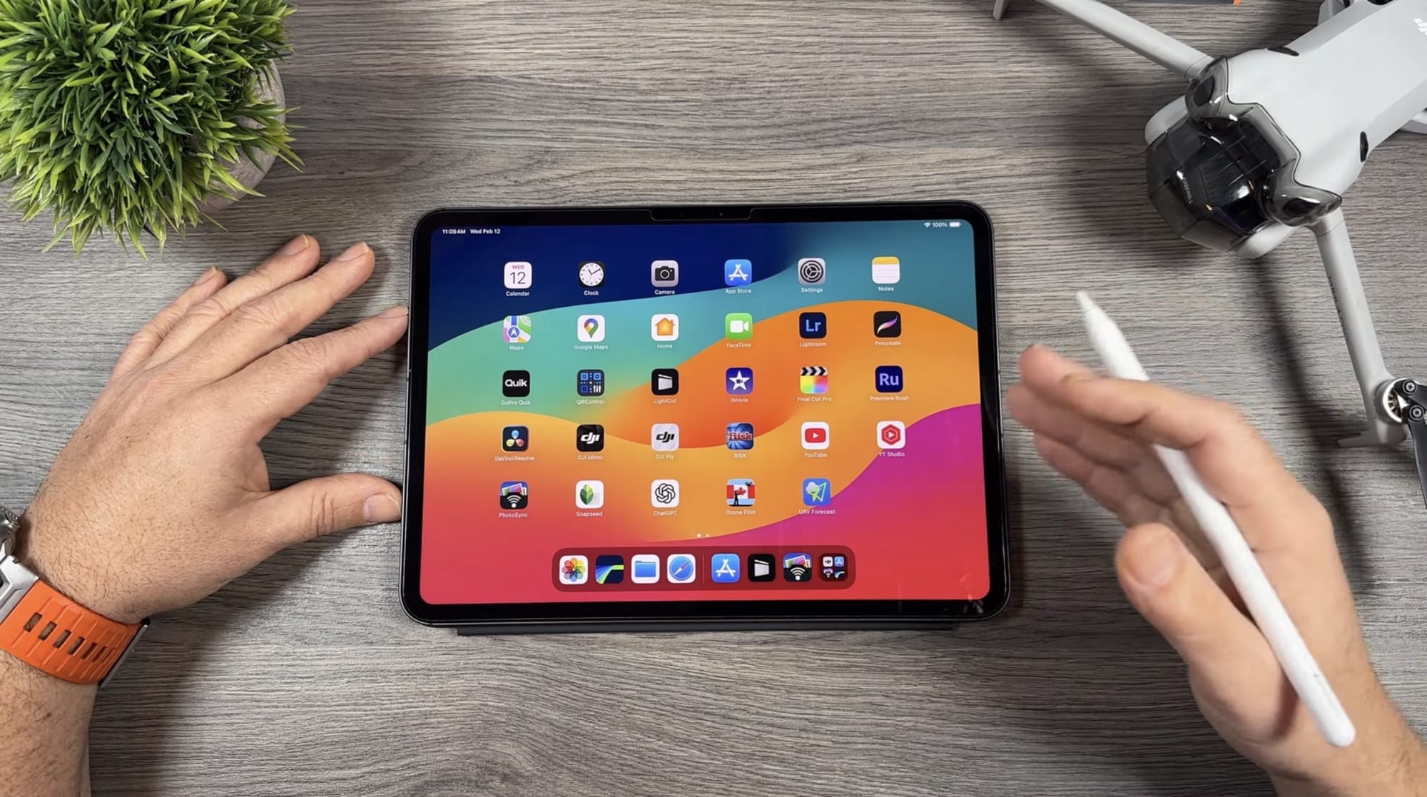 Hands at a tablet home screen with a folded drone on the desk.