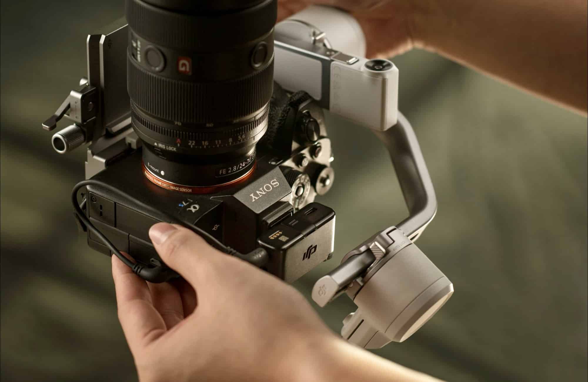 Hands balance a Sony body and long lens on the gimbal quick-release plate.