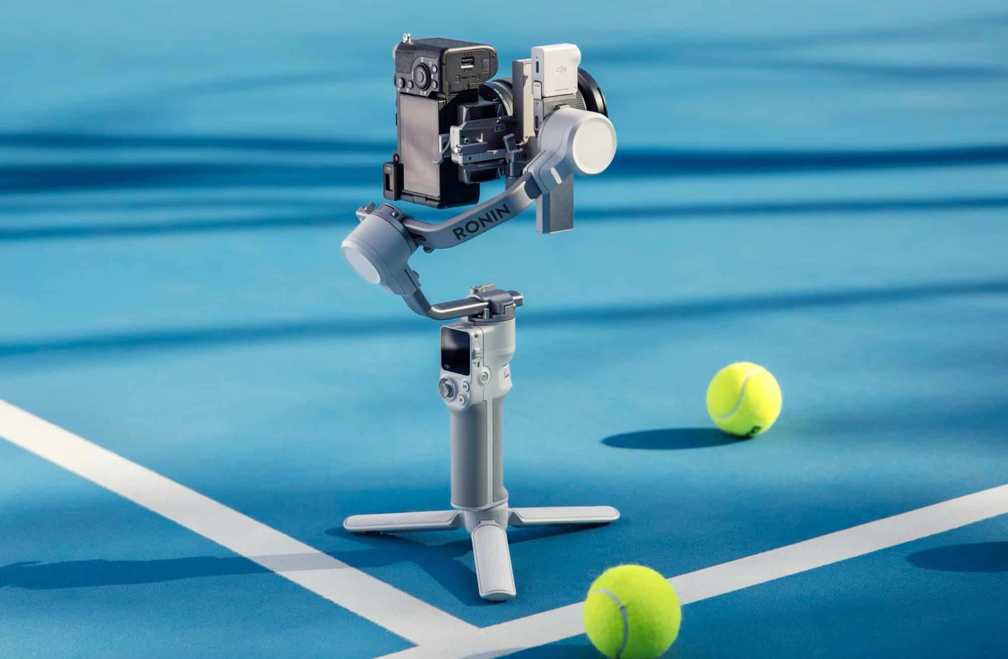 The gimbal stands on its tripod on a blue tennis court among loose balls.