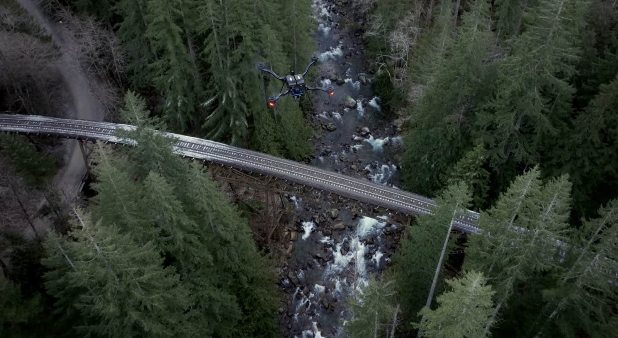 Aerial view of the drone tracking a trestle bridge over a forested creek.