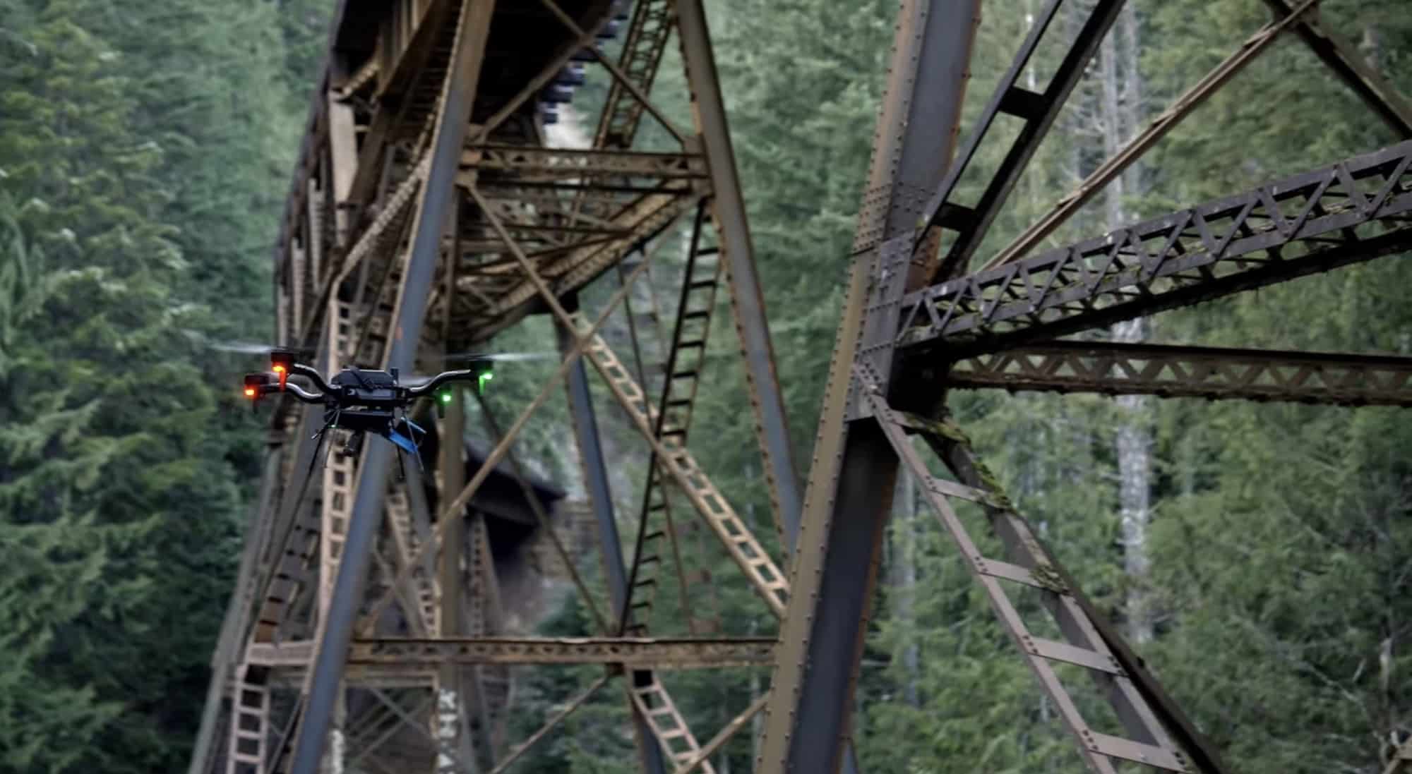 A drone flies inside the steel latticework of a railway trestle in the forest.
