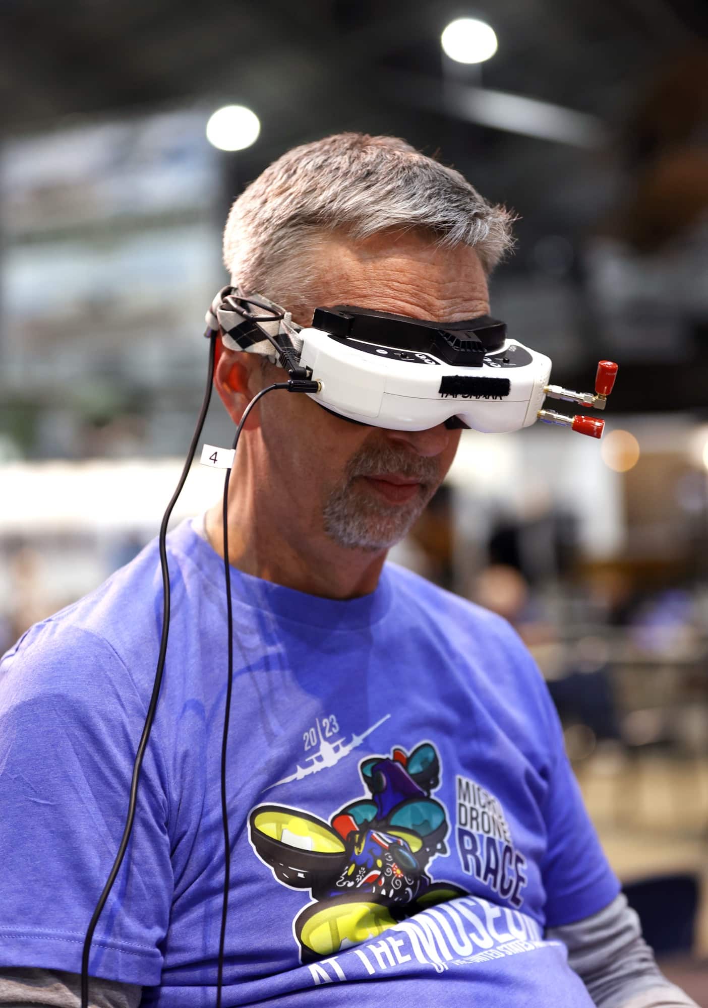 A grey-haired spectator wears first-person-view goggles inside the museum hall.