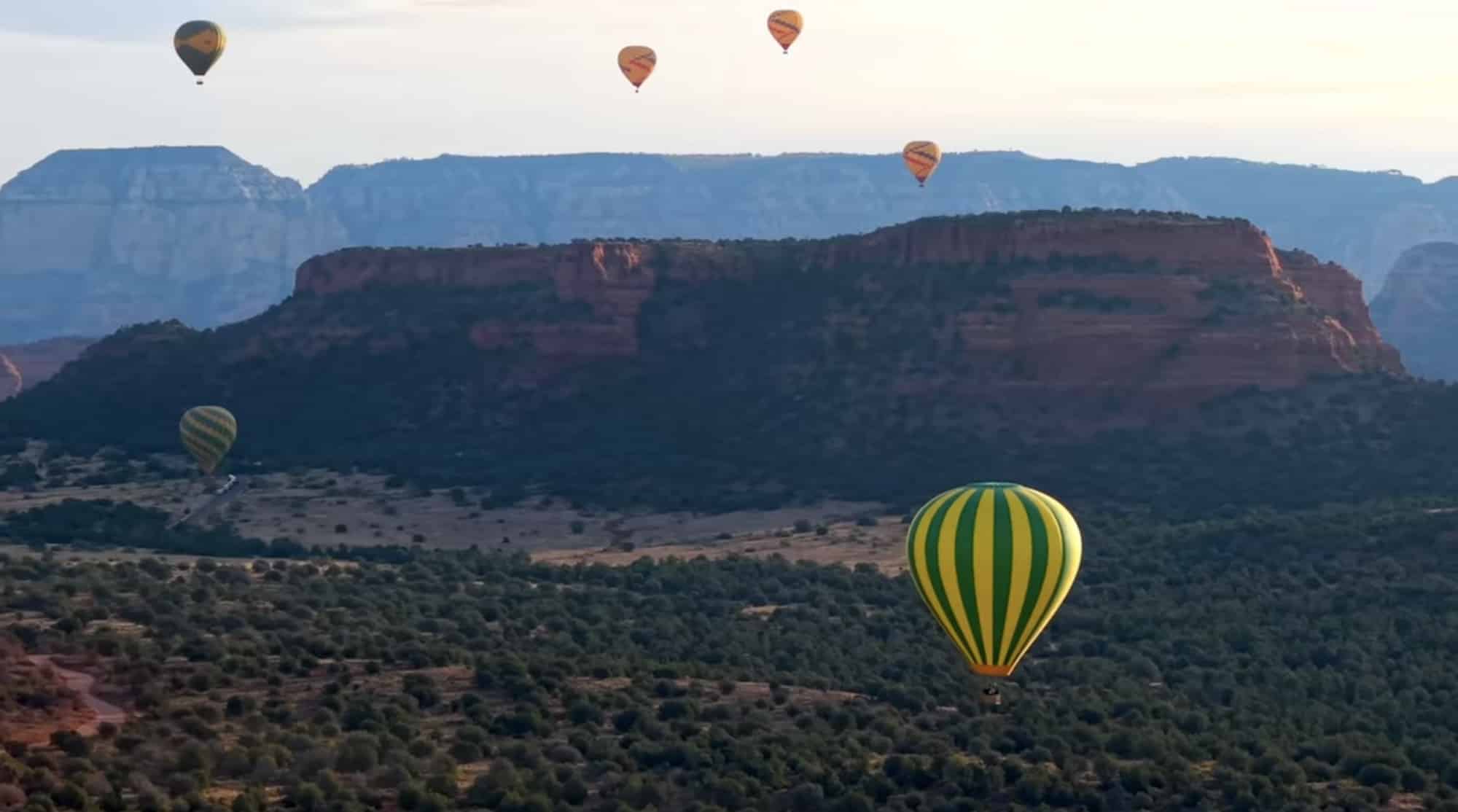 Hot air balloons drifting over red rock mesas and green pinyon woodland.