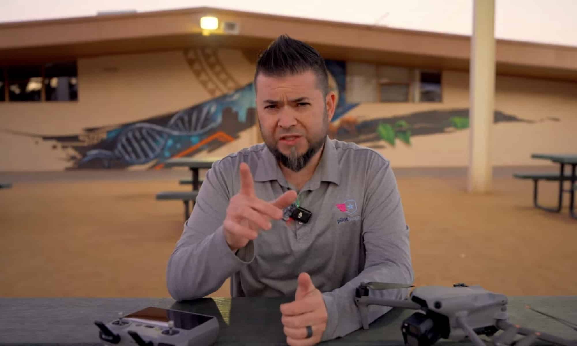 Reviewer talking to camera outdoors with the drone and controller on the table.