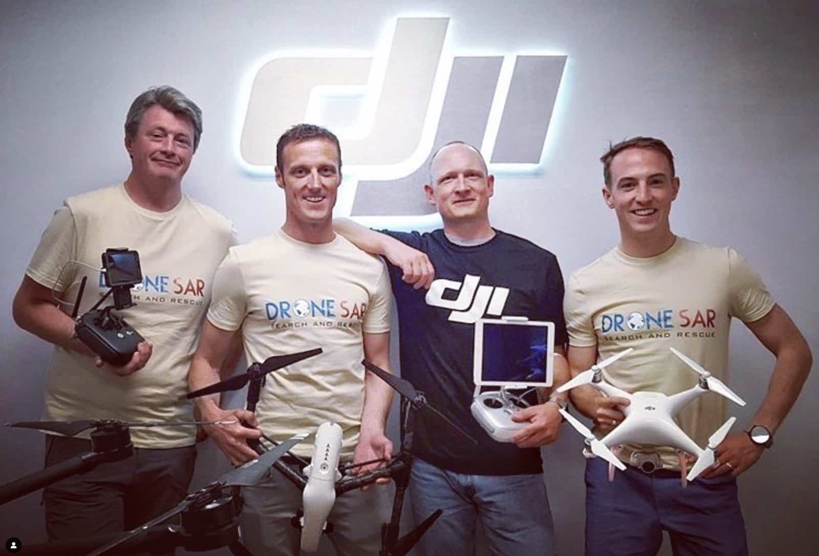 Four men holding Phantom quadcopters and controllers pose beneath an illuminated DJI logo.