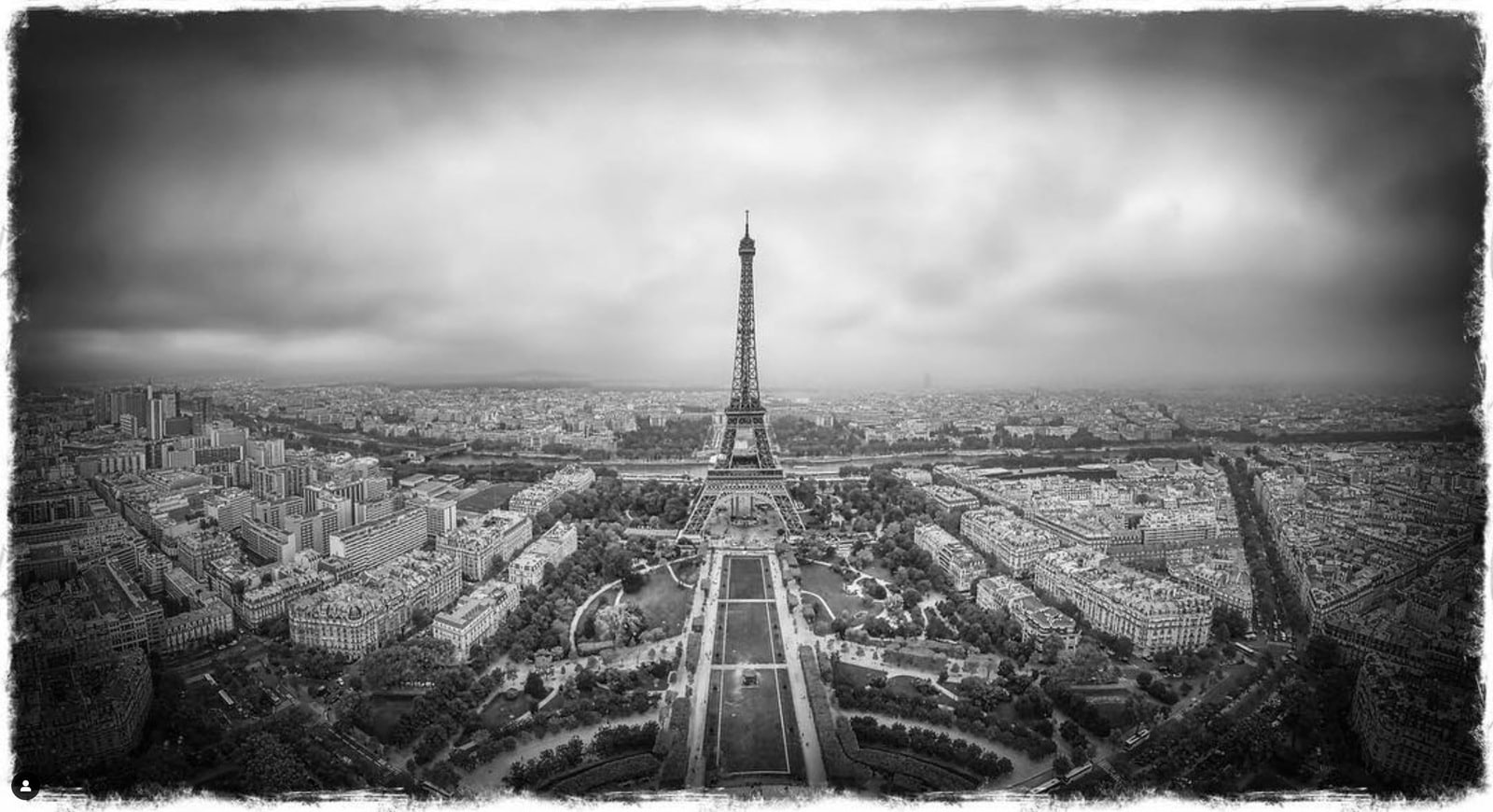 A black-and-white aerial panorama of Paris centered on the Eiffel Tower.