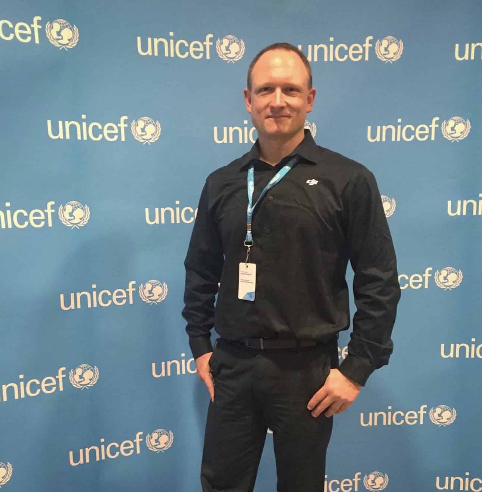 A lanyard-wearing delegate stands in front of a UNICEF step-and-repeat backdrop.