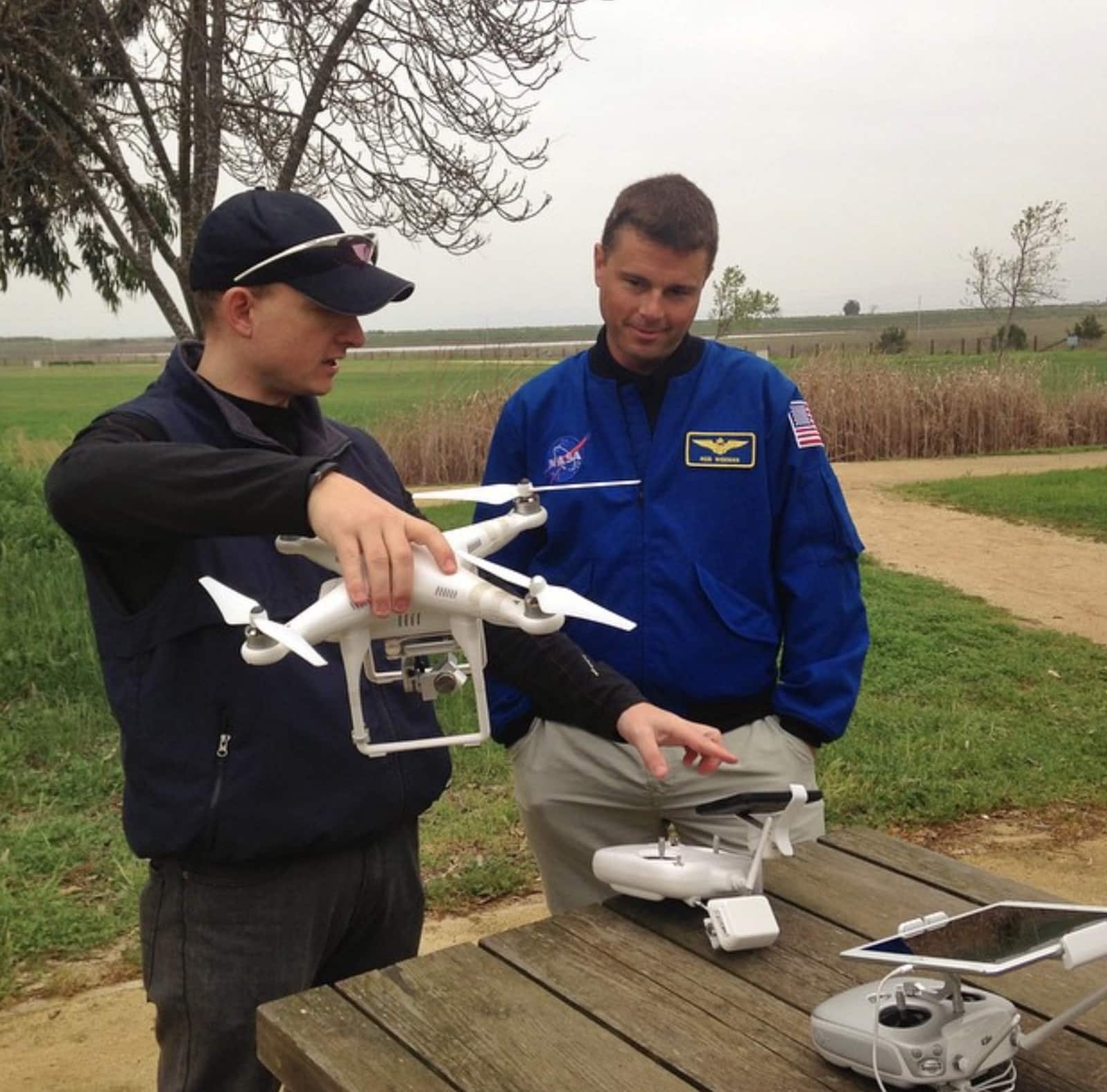 Two men inspect a DJI Phantom on a picnic table, one in a NASA flight jacket.