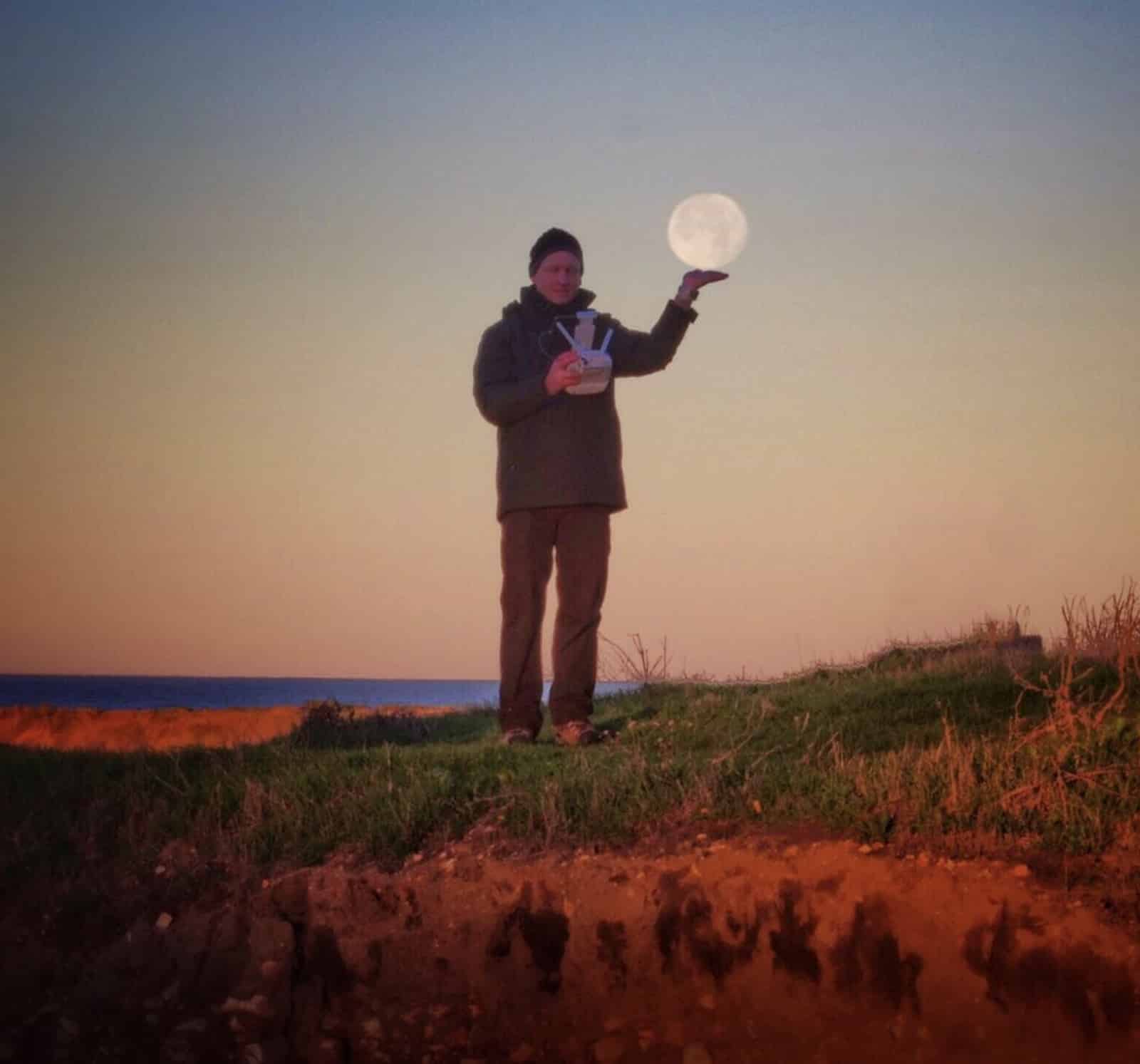 Forced-perspective sunset shot of a man appearing to balance the moon on his hand.