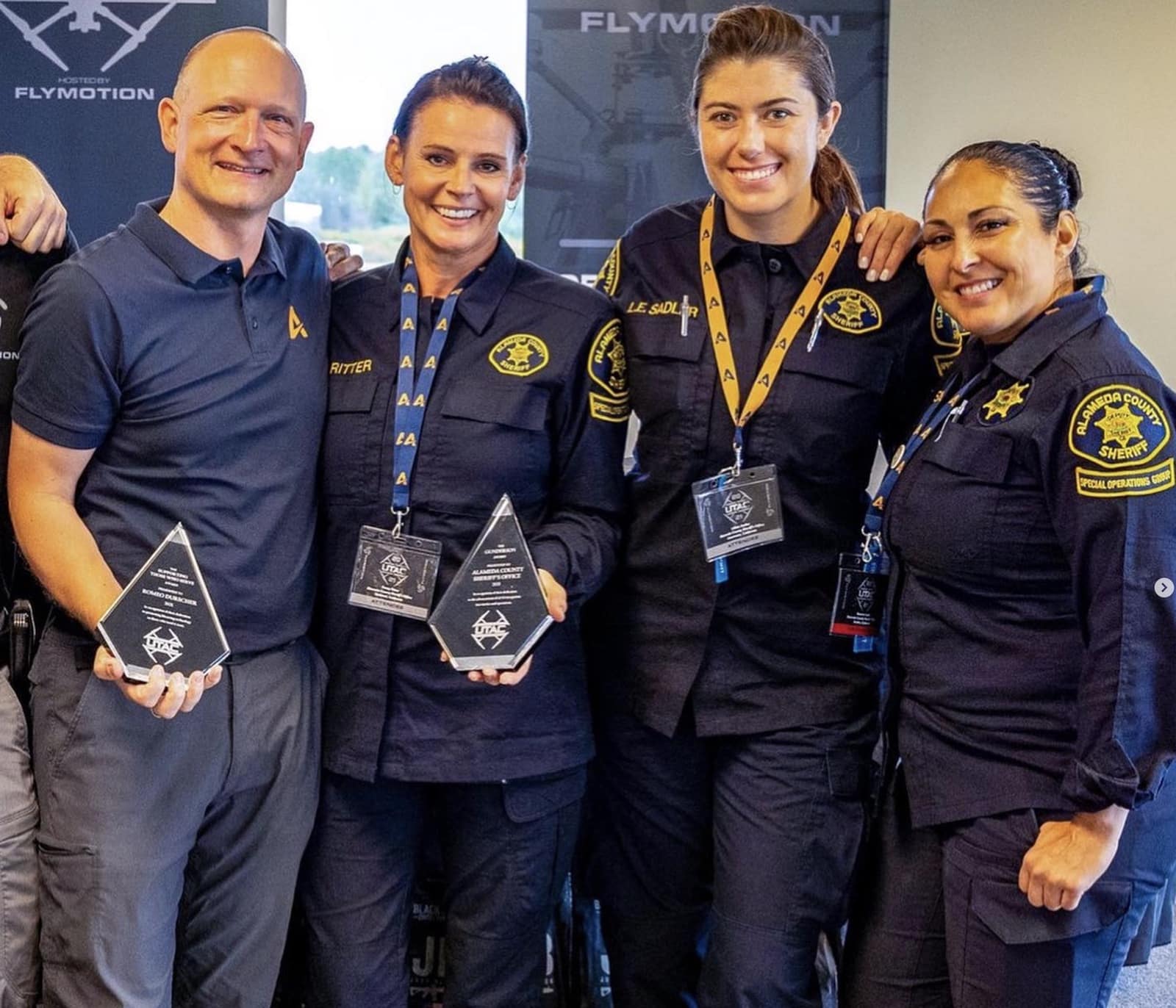 A man in an Auterion polo stands with three uniformed deputies holding glass awards.