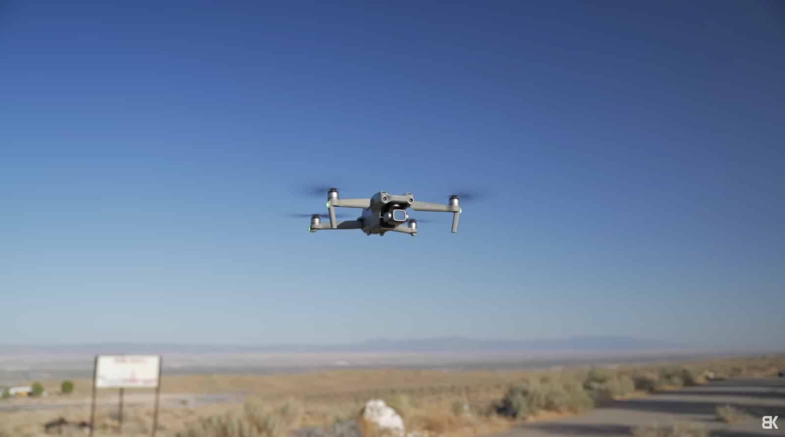 A small quadcopter hovers above dry scrub beside a desert road.