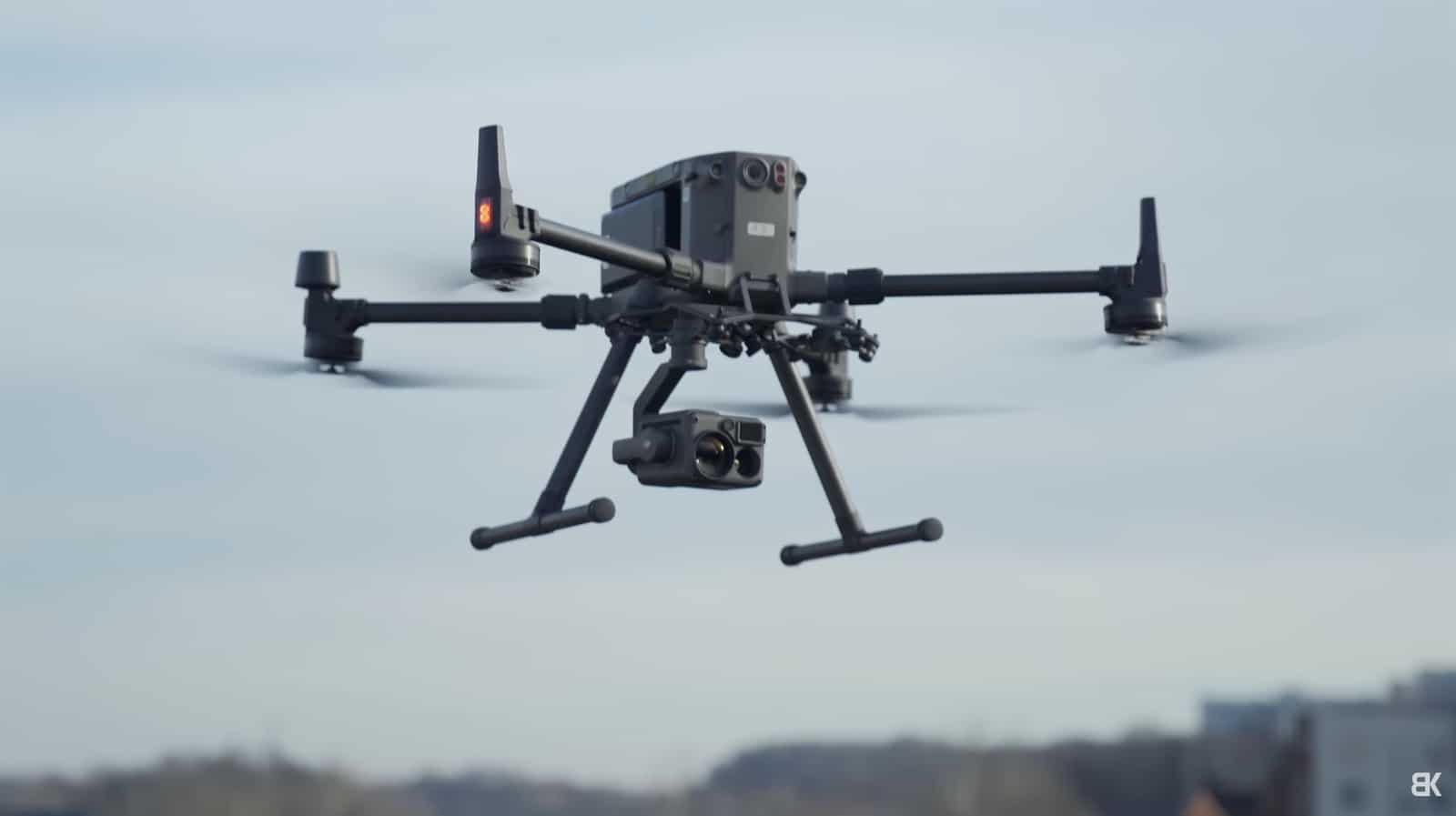 An enterprise quadcopter hovers with a gimbal payload above distant rooftops.