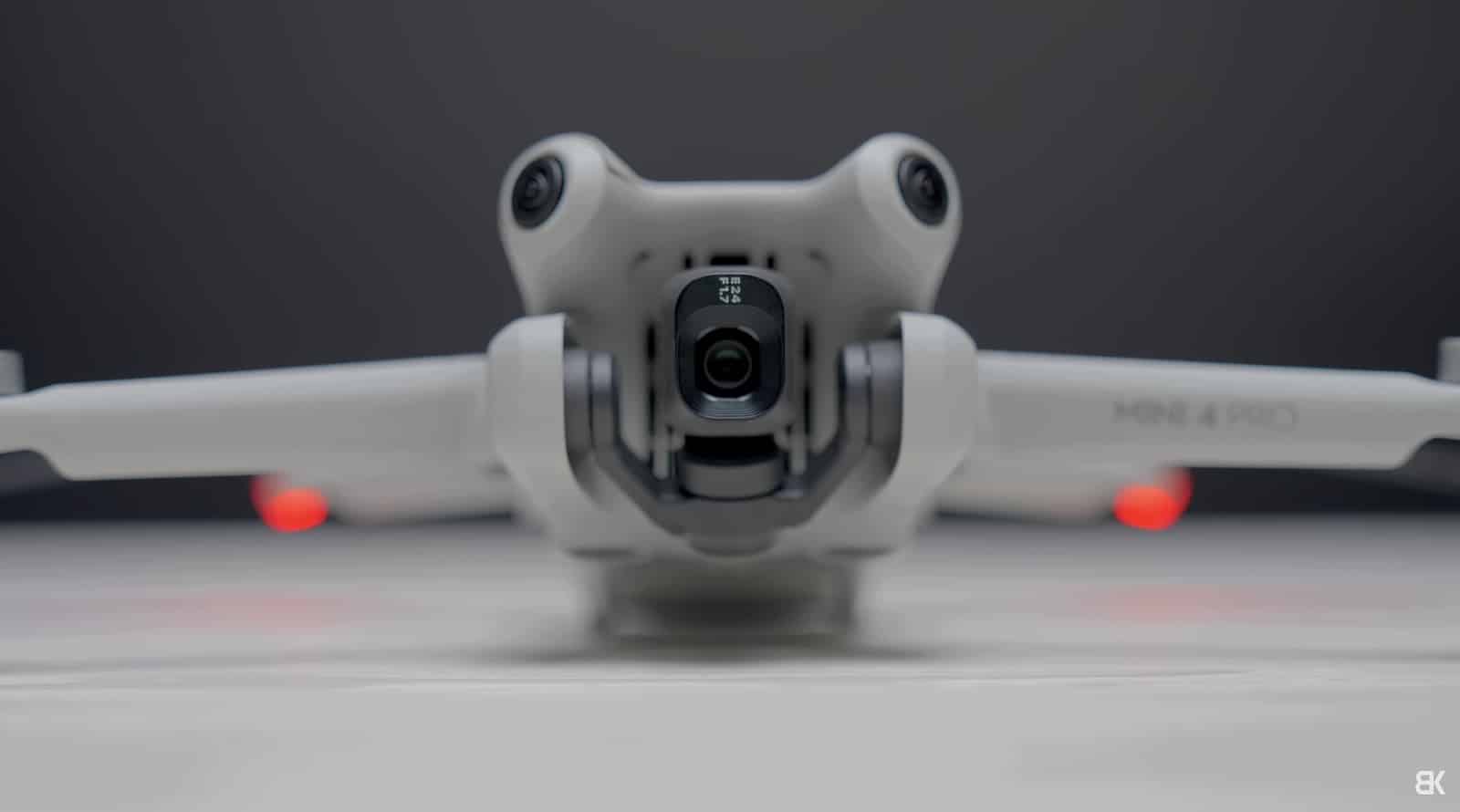 A DJI Mini 4 Pro head-on with red navigation lights glowing.